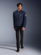 Male model wearing Alpinestars Bruiser Jacket in Dark Blue, urban textile motorcycle jacket, paired with black pants and black sneakers, workwear-inspired aesthetic with zippered pockets and circular sleeve patch, contemporary streetwear for motorcycle riding.