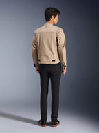 Alpinestars Bruiser Jacket i brun, urban motorcykeljakke set bagfra på model, arbejdstøjsinspireret design med metaløskner på ryggen og taljejusteringer, kombineret med sorte bukser og sneakers, moderne street-kørestil.