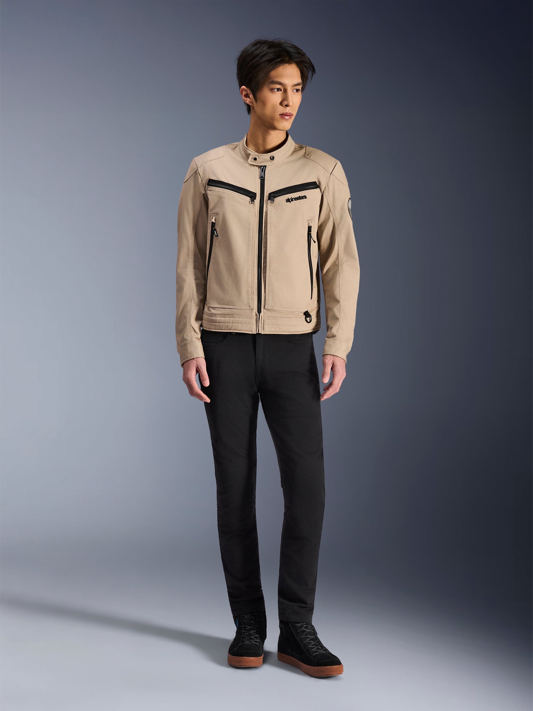 Alpinestars Bruiser-jakke, urban motorcykeljakke i farven Aluminum, kombineret med sorte bukser og sorte sneakers, med sorte lynlåslommer og krave med trykknap, moderne arbejdstøj-inspireret design til bykørsel