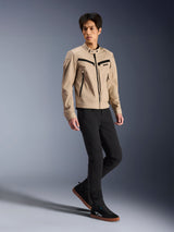 Alpinestars Bruiser-jakke, urban motorcykeljakke, tan, båret af en mandlig model med sorte slim-fit bukser og sorte sneakers, arbejdstøjsinspireret tekstilkonstruktion med sorte lynlåsdetaljer, moderne urban street-stil.