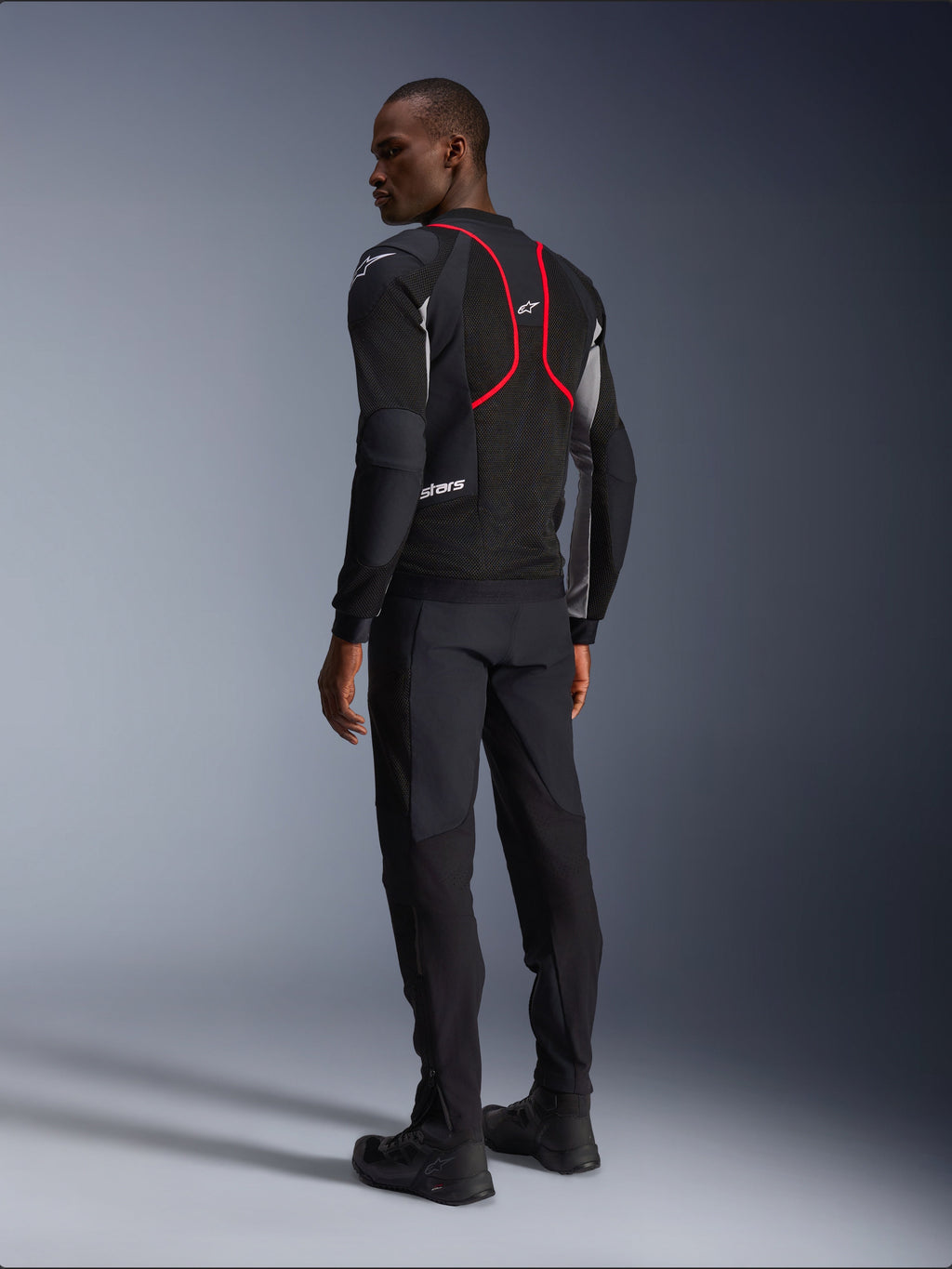Alpinestars Troop-Air Pro-jakke, motorcykeljakke, sort, askegrå og lysende rød, set bagfra på model, med røde accentlinjer og mesh-ventilationspaneler, båret med sorte bukser og støvler, urban motorcykelstil