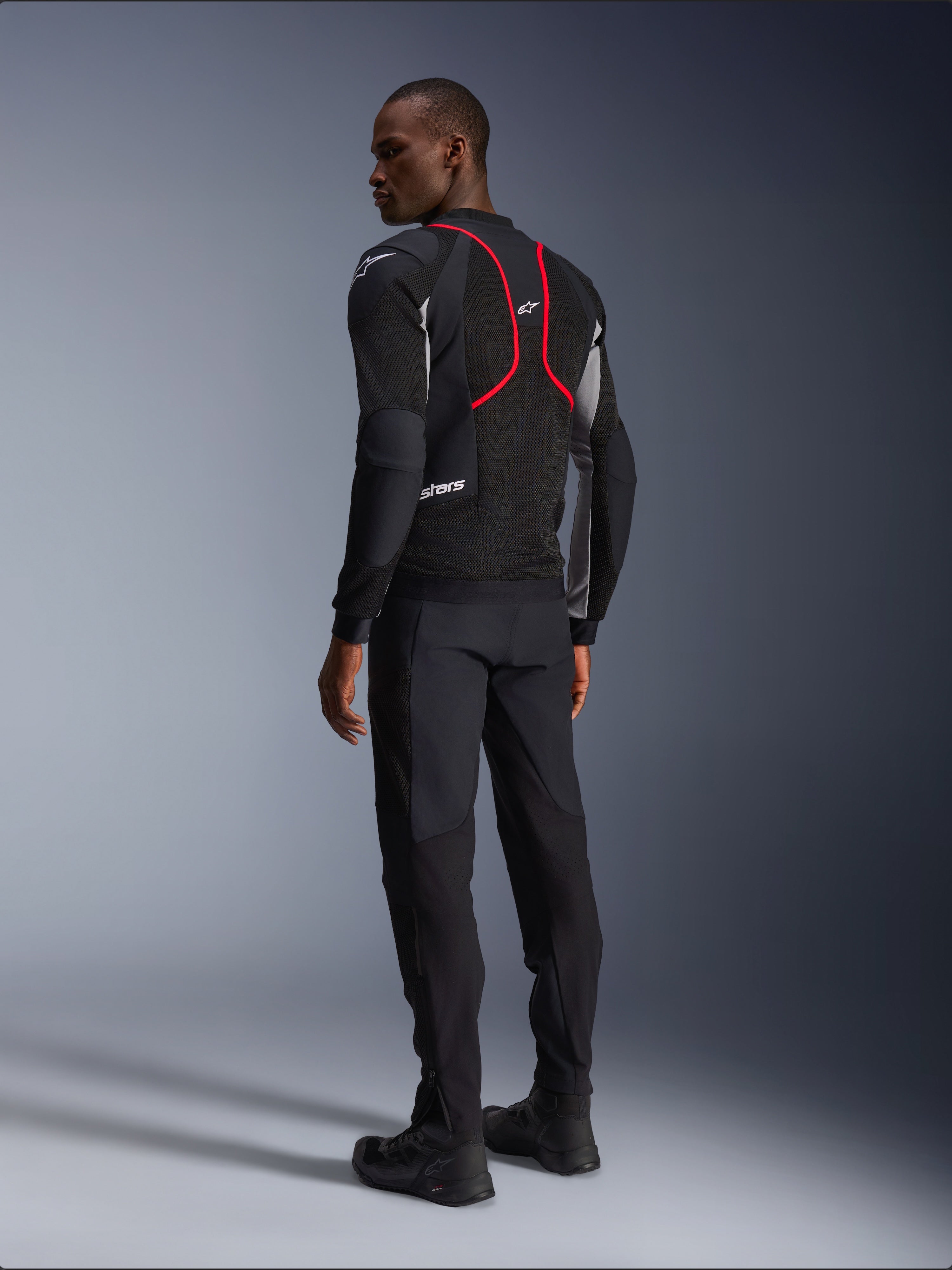 Alpinestars Troop-Air Pro-jakke, motorcykeljakke, sort, askegrå og lysende rød, set bagfra på model, med røde accentlinjer og mesh-ventilationspaneler, båret med sorte bukser og støvler, urban motorcykelstil