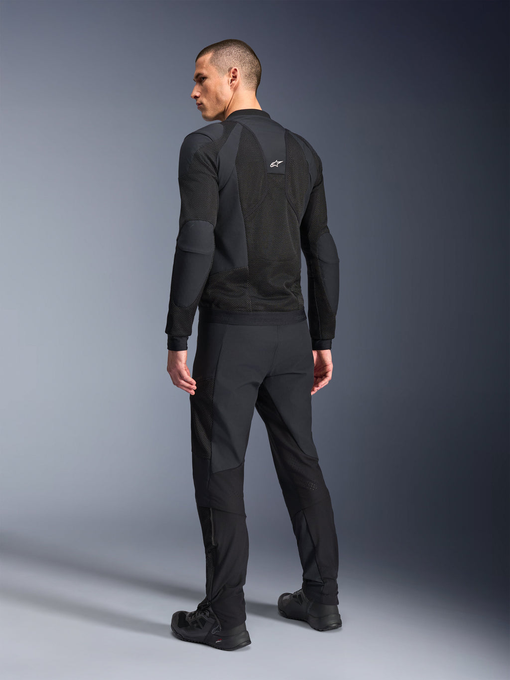 Alpinestars Troop-Air Pro-jakke, sort, teknisk pansret luftjakke set bagfra, med omfattende mesh-paneler til luftgennemstrømning, kombineret med matchende sorte tekniske bukser og sko.