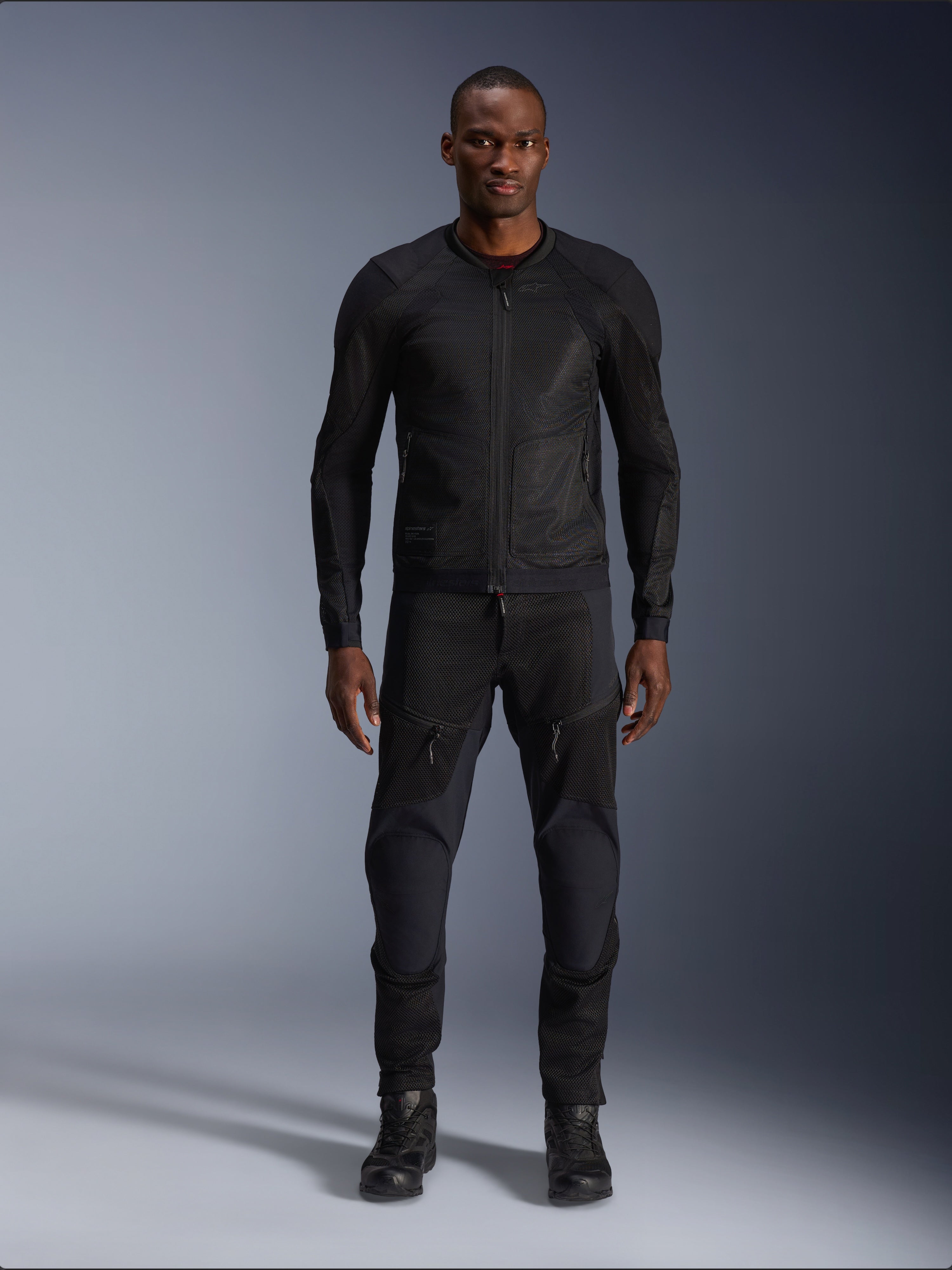 Male model wearing the Alpinestars Troop-Air Jacket in Black Black, lightweight mesh motorcycle jacket, paired with matching black riding pants and boots, featuring a technical 2D tech mesh construction for superior airflow.