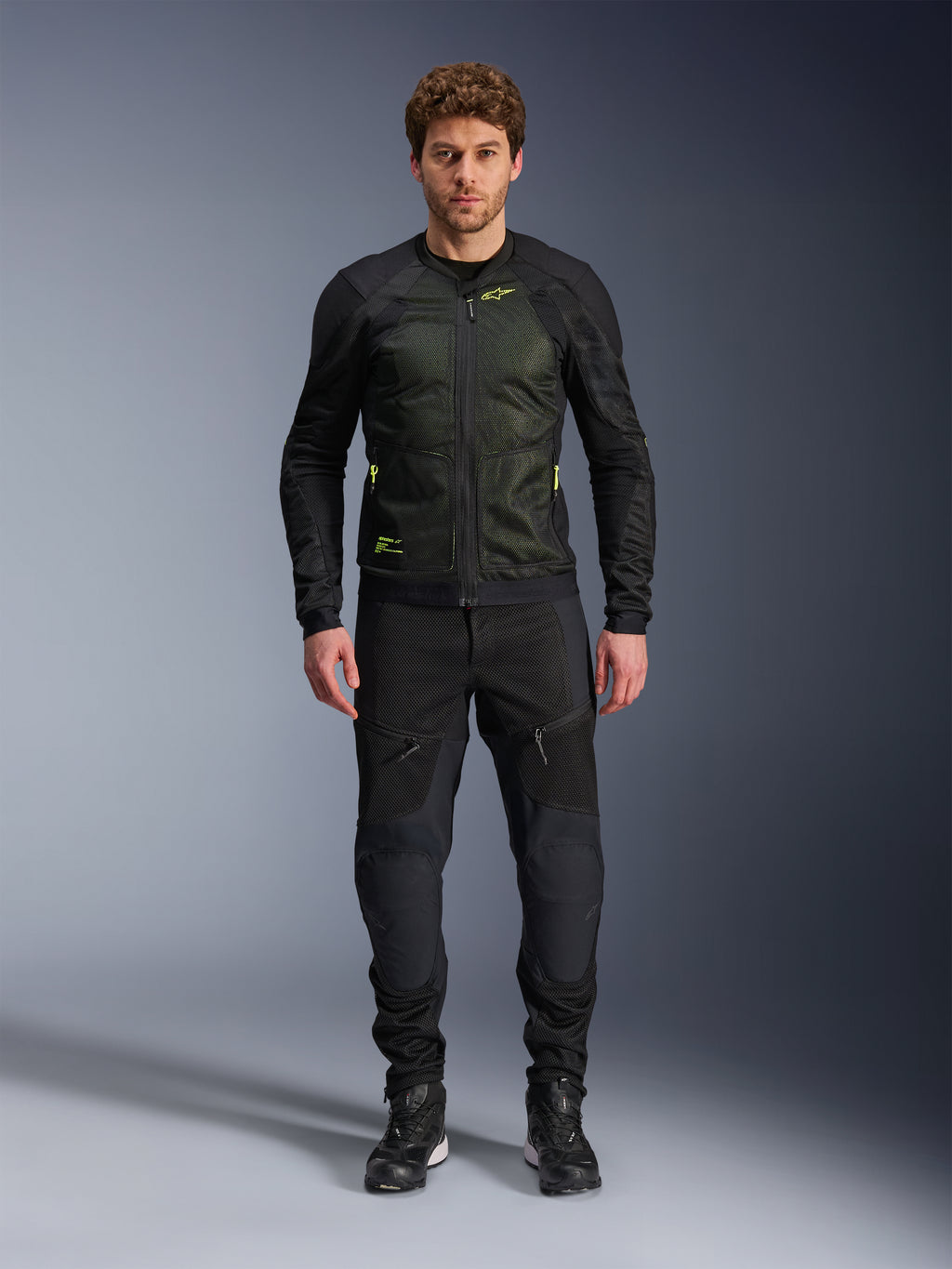 Male model wearing Alpinestars Troop-Air Jacket in Black Yellow Fluo, featuring technical mesh panels and bright yellow accents, paired with black riding pants and shoes, contemporary motorcycle apparel for warm weather