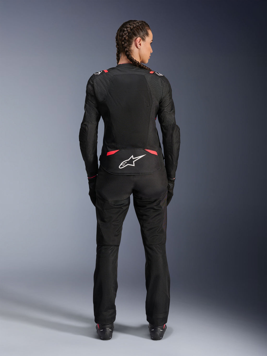 Alpinestars Stella T-SPS Air V2-jakke, motorcykeljakke i tekstil til kvinder, sort og Diva Pink, set bagfra på model med flettet hår, med store mesh-paneler til ventilation, hvidt Astars-logo på lænden, kombineret med matchende sorte kørebukser.
