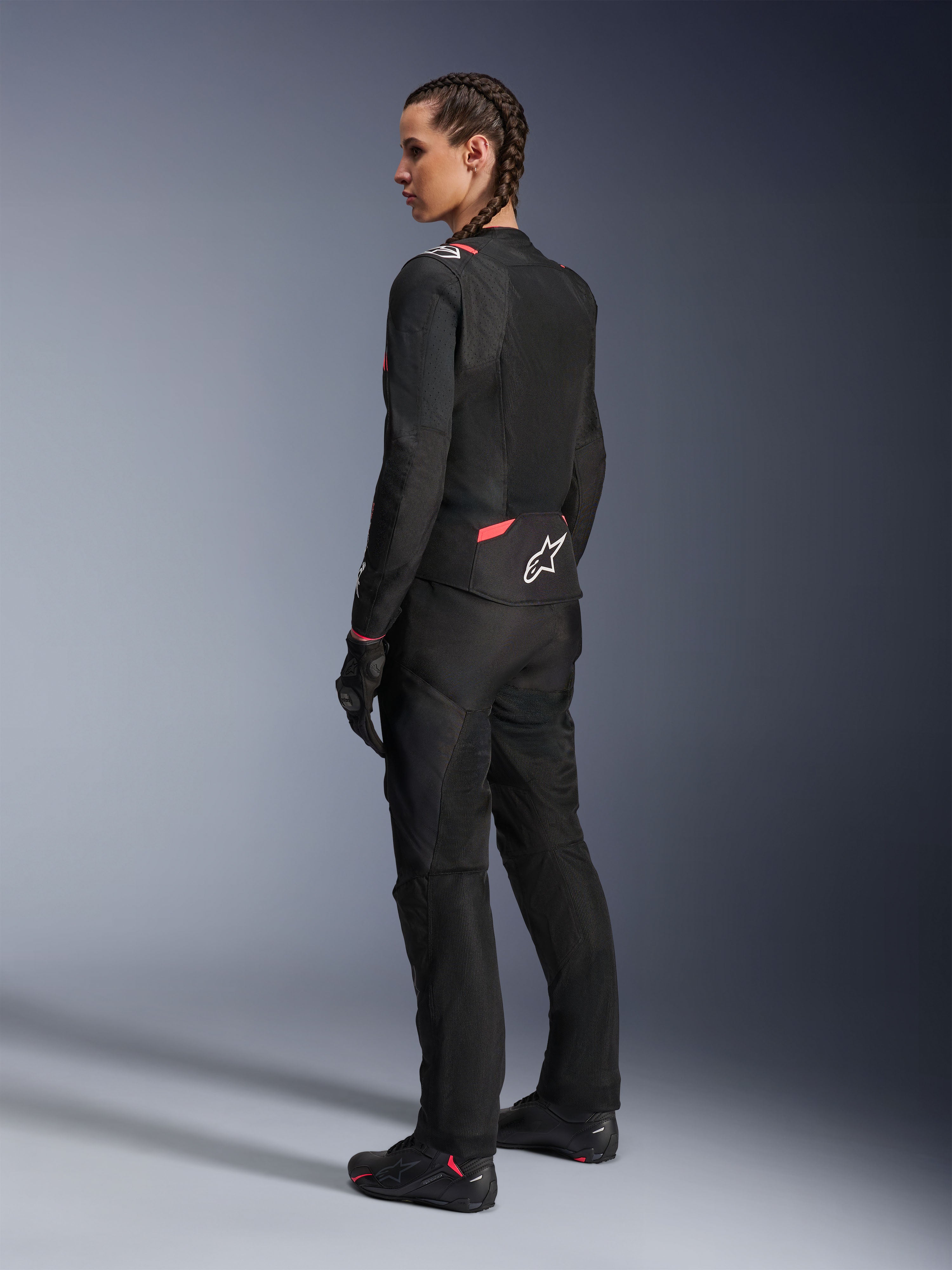 Alpinestars Stella T-Sps Air v2 jakke til damer, sort og Diva Pink, tekstil motorcykeljakke vist fra siden bagfra, store mesh-paneler for ventilation, hvidt stjernelogo på ryggen, båret med matchende sorte kørebukser, handsker og støvler