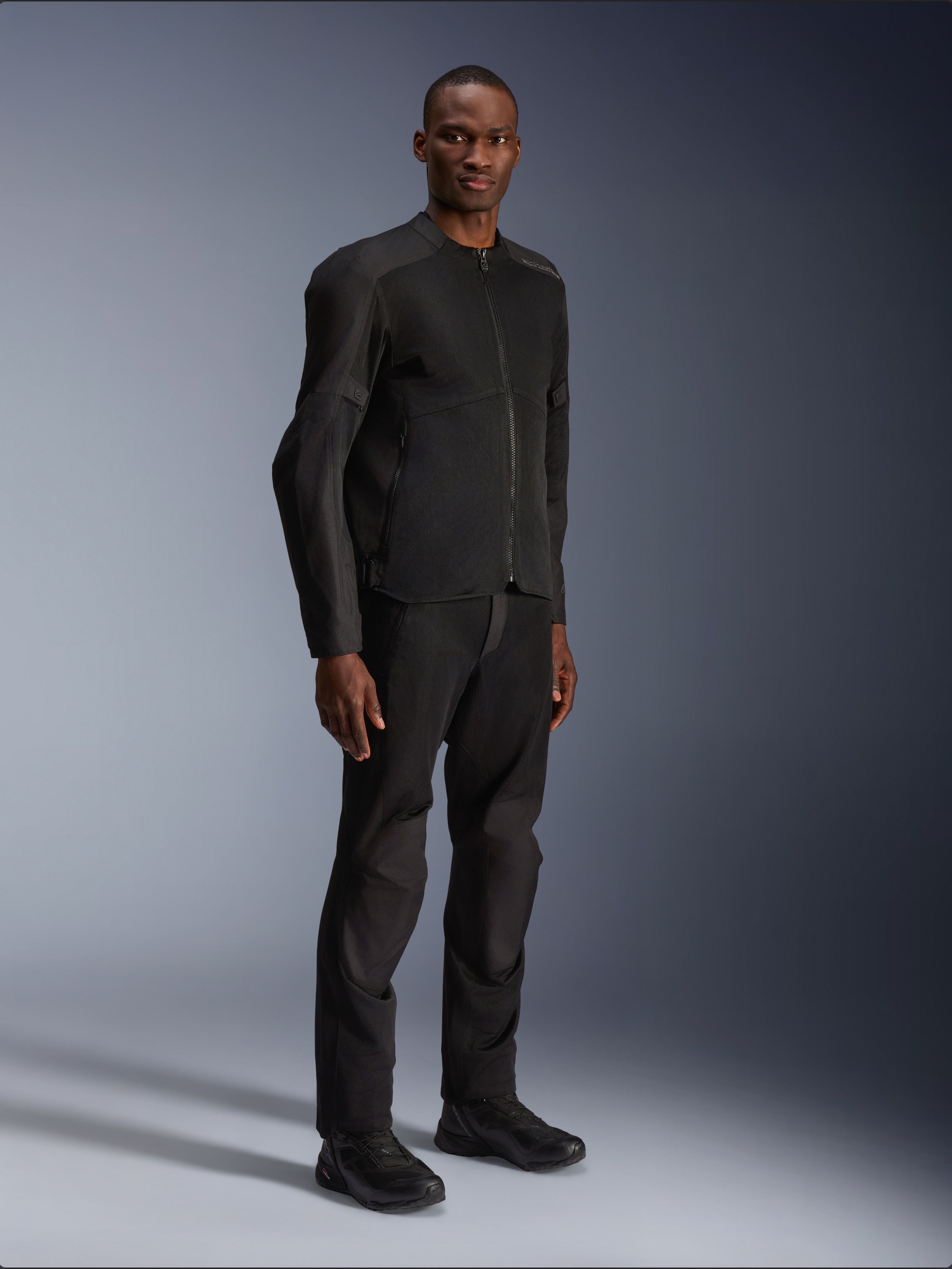 Alpinestars C-1 Air-jakke, sort, båret af en model med matchende sorte motorcykelbukser og sko, store tech mesh-paneler for luftgennemstrømning, ren urban æstetik med en strømlinet pasform