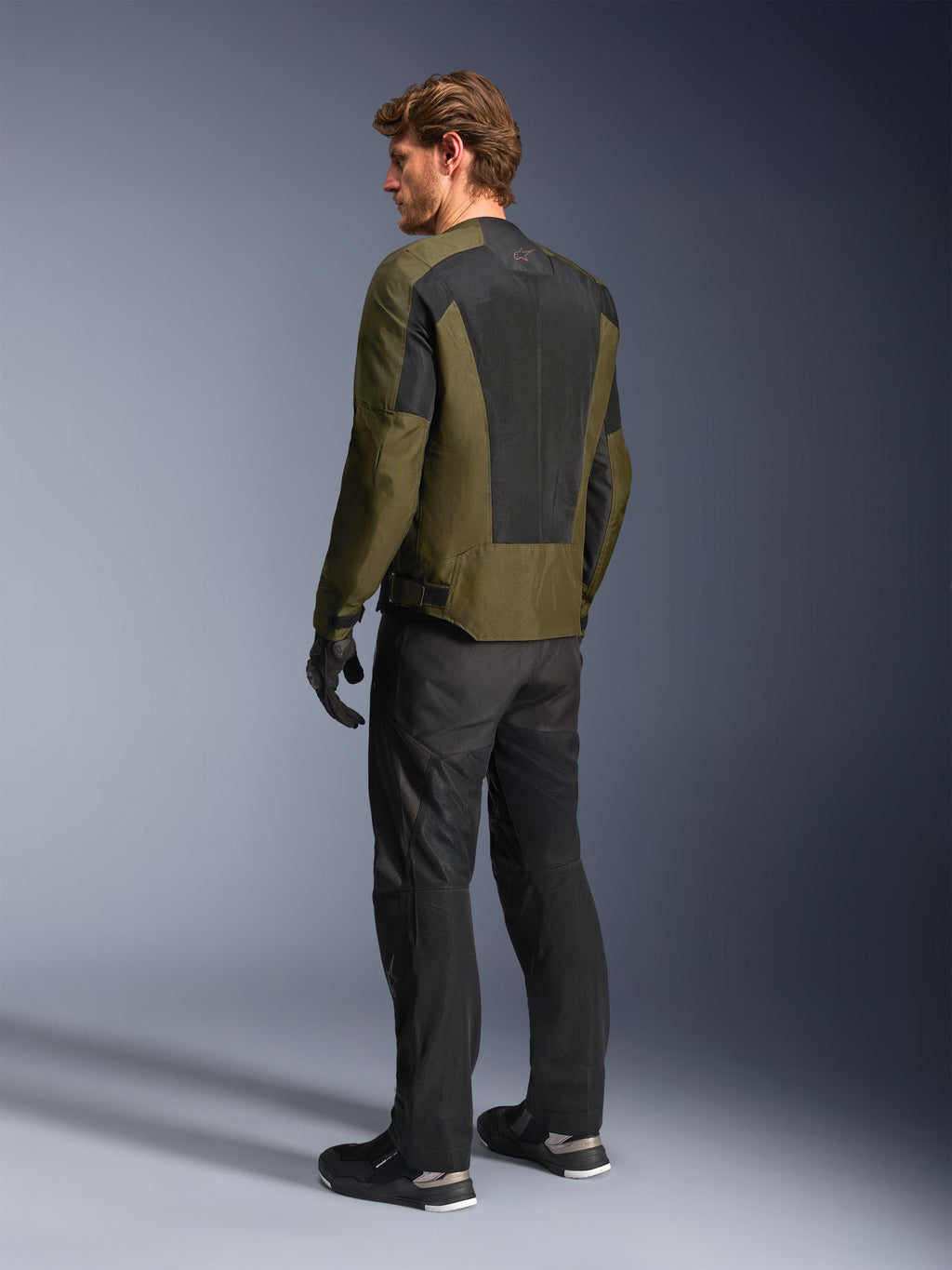Mandlig model iført Alpinestars C-1 Air-jakke i Khaki, urban motorcykeljakke, set bagfra med fokus på store sorte mesh-paneler på ryggen, sorte tekniske kørebukser og handsker, moderne motorcykeludstyr til varmt vejr