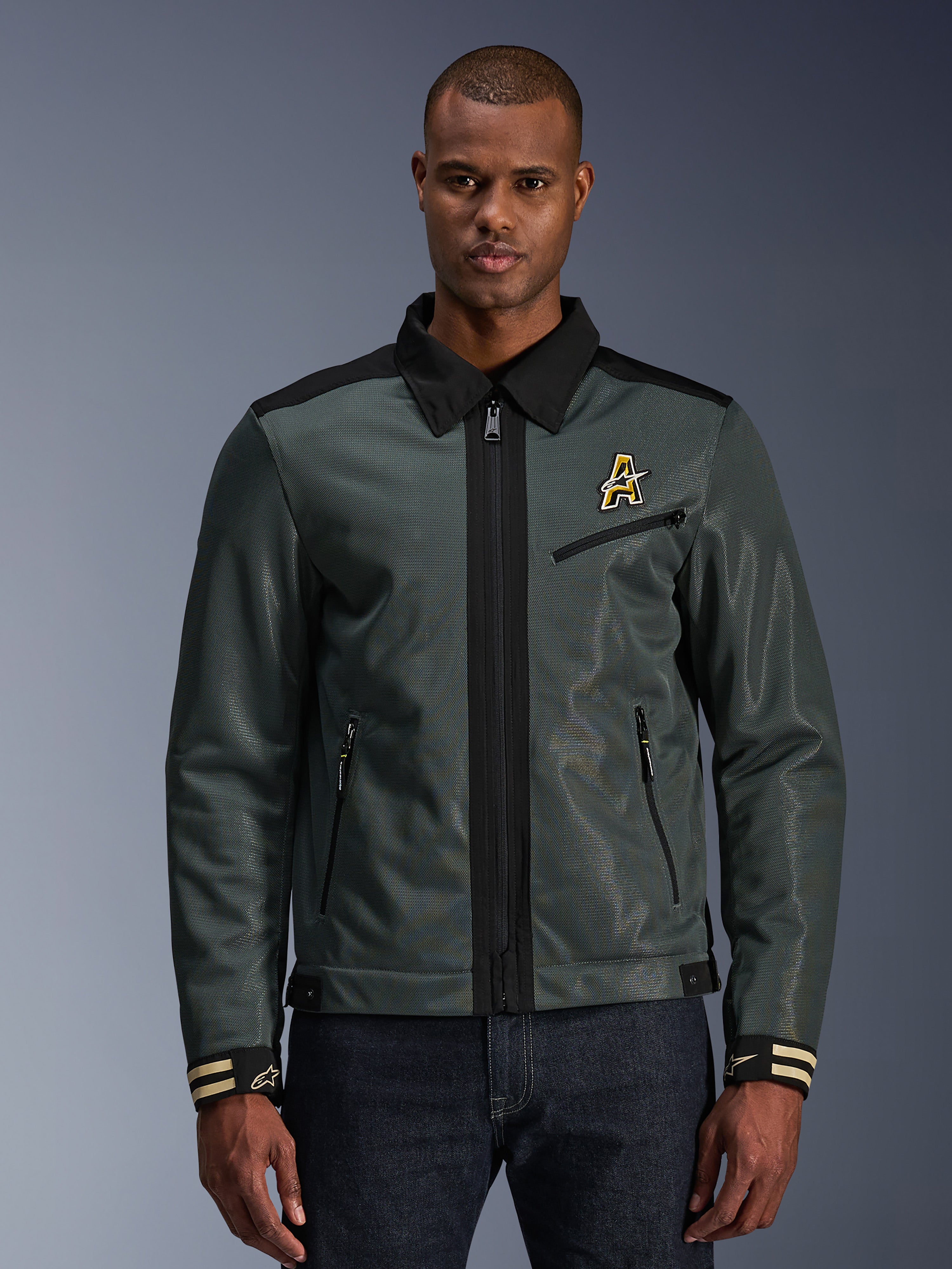 Alpinestars Ignite Air jakke, urban motorcykeljakke, mørk skovgrøn med sorte detaljer, vist på model med denimbukser, Harrington-inspireret skjortekrave, lynlås foran, logo på brystet og stribede manchetter, moderne mesh- og tekstilkonstruktion til sommerkørsel