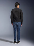 Set bagfra af en model iført Alpinestars Provoke Jacket, sort teknisk tekstil-motorcykeljakke, kombineret med blå denim-kørejeans og sorte sneakers, der viser rykkonstruktionen og et lille hvidt Alpinestars-logo, moderne urbant design