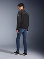 Alpinestars Provoke-jakke, sort urban motorcykeljakke, båret af en model i trekvart profil bagfra, kombineret med blå denimjeans og sorte sneakers, med ripstop softshell-indsatser og hvidt Alpinestars-branding på ærmet og ryggen.