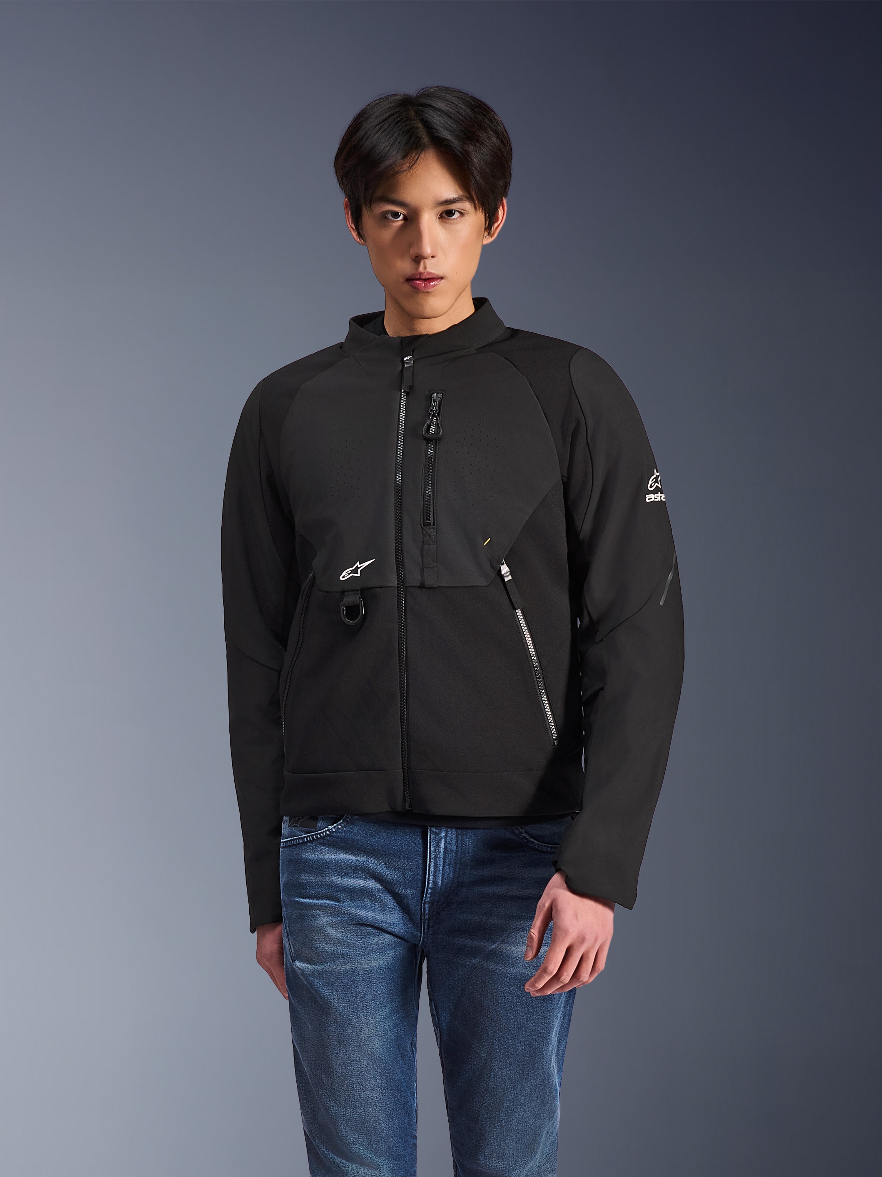 Alpinestars Provoke jakke, sort tekstiljakke til urban kørsel, båret af en mandlig model med blå jeans, med laserperforerede brystpaneler, flere lynlåslommer, hvidt A-star logo på brystet og ærmet, strømlinet moderne design til bykørsel