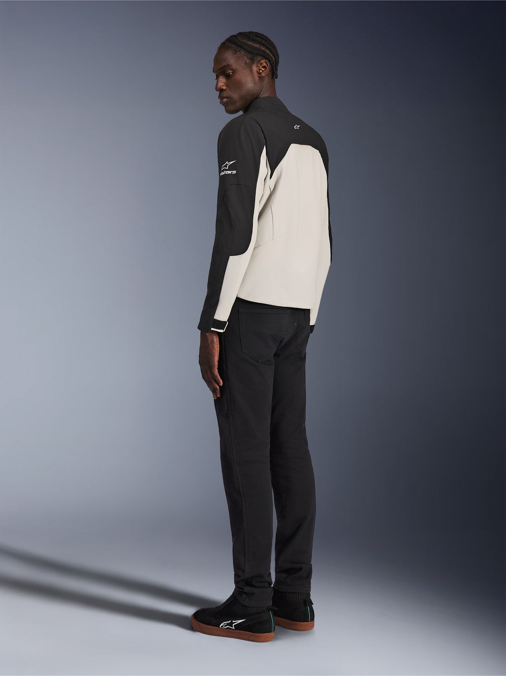 Alpinestars Provoke jakke, urban motorcykeljakke, sort og metalgrå, set bagfra i trekvart profil på en model, totonet tekstilkonstruktion med Alpinestars-logo på skulderen, båret med sorte bukser og sorte sneakers, moderne gadeklar beskyttelse