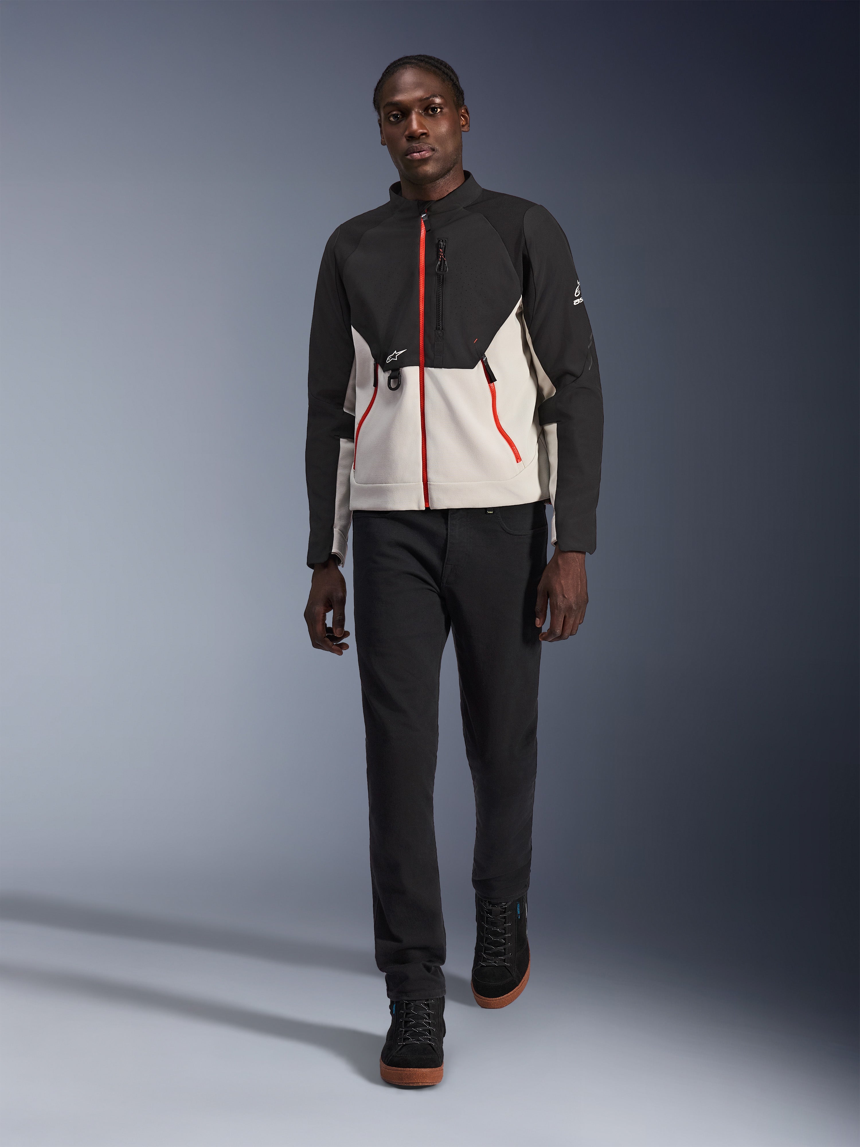 Mandlig model iført Alpinestars Provoke-jakken, urban motorcykeljakke i sort og metalgrå med røde lynlåsdetaljer, kombineret med sorte bukser og sorte high-top sko, moderne gadeklart beskyttelsesudstyr til bykørsel