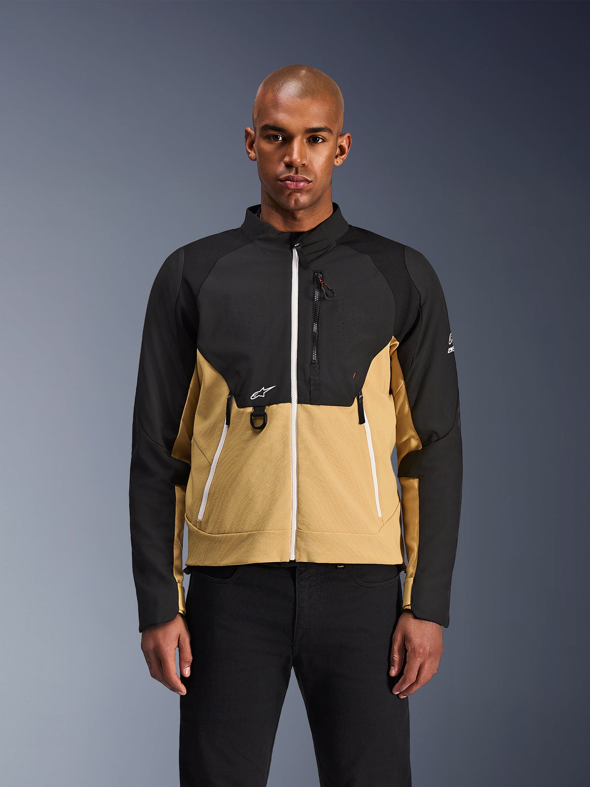 Alpinestars Provoke-jakke, urban motorcykeljakke, sort og camel, set forfra på en mandlig model, med et tofarvet design med hvide lynlåse, brystlomme med lynlås og D-ring og lille hvidt Alpinestars-logo, moderne urbant rytterudstyr
