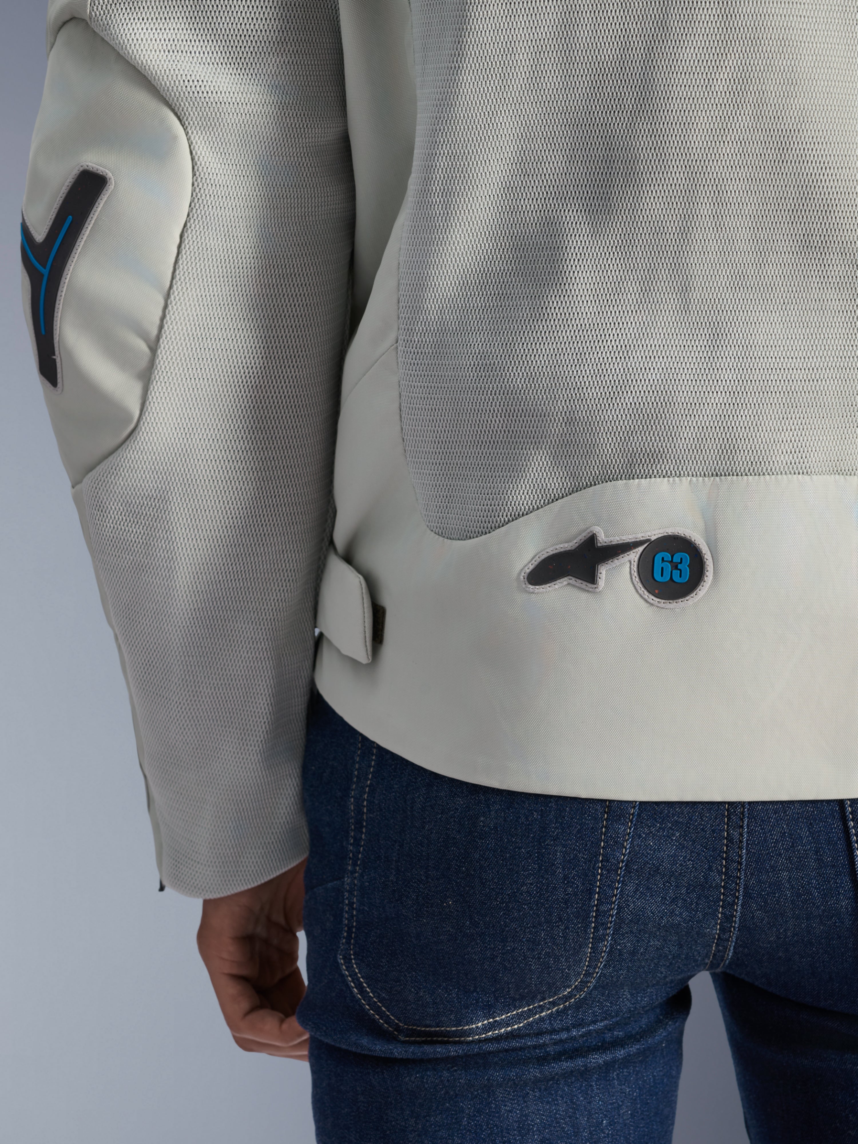 Alpinestars Circal-1 Air Jacket i Metal Gray med Methyl Blue-accenter, detaljeret set bagfra, der fremhæver luftpaneler i genanvendt mesh og et rundt '63'-logomærke, båret med blå jeans.
