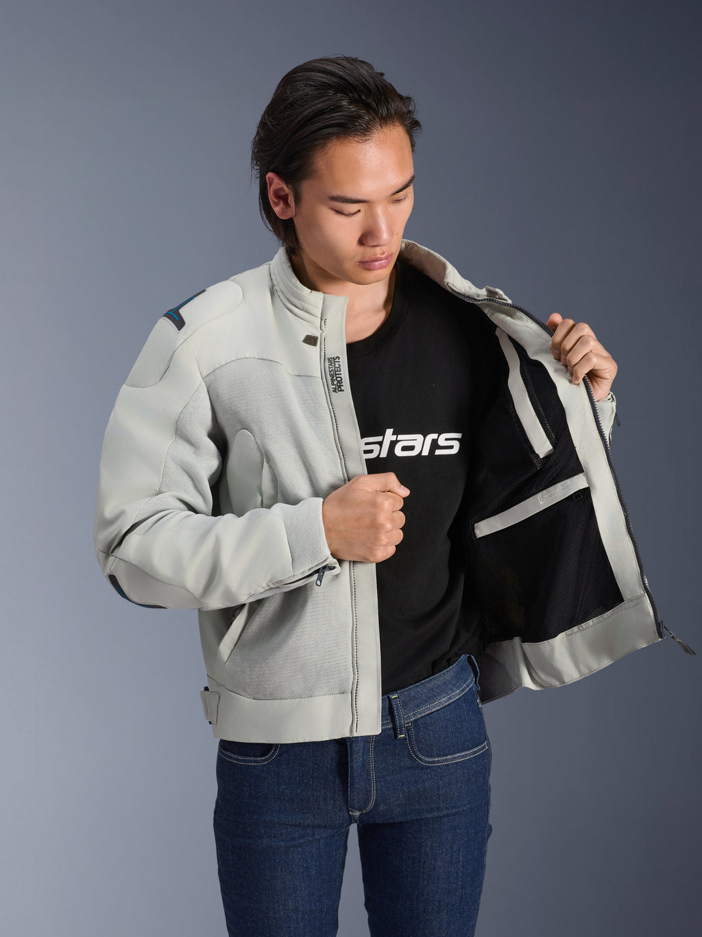 Alpinestars Circal-1 Air jakke, metalgrå, holdt åben for at vise indvendigt mesh-foer og lommedetaljer, båret af en model med en sort t-shirt med logo og blå jeans, urban motorcykelstil