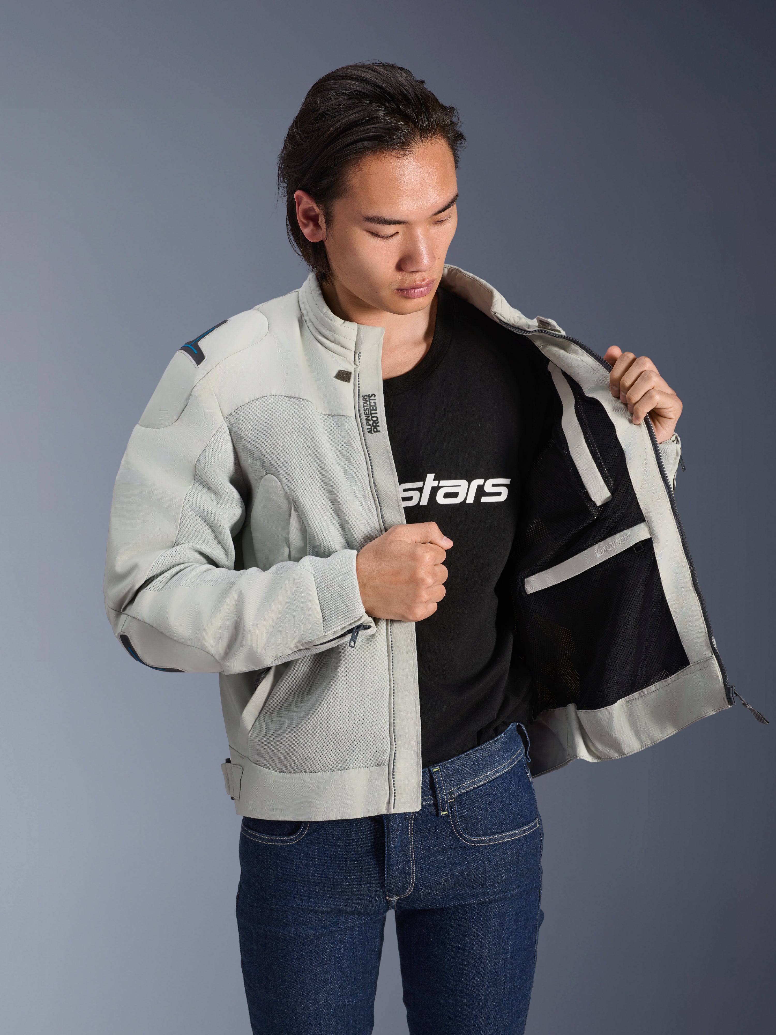Alpinestars Circal-1 Air jakke, metalgrå, holdt åben for at vise indvendigt mesh-foer og lommedetaljer, båret af en model med en sort t-shirt med logo og blå jeans, urban motorcykelstil