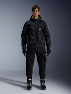 Mandlig model iført Alpinestars Mogress Air-jakke, sort tekstiljakke med hætte og lime punch-detaljer, sorte utility-bukser, sorte handsker og sort-hvide kørestøvler, urbant motorsport-inspireret streetwear-design