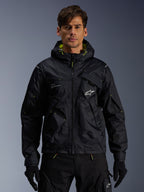 Alpinestars Mogress Air-jakke, urban motorcykeljakke, sort med Lime Punch-detaljer, båret af en model med sorte kørebukser og handsker, utility-inspireret design med hætte og hvidt stjernelogo på brystet, letvægts tekstiludstyr til gadekørsel