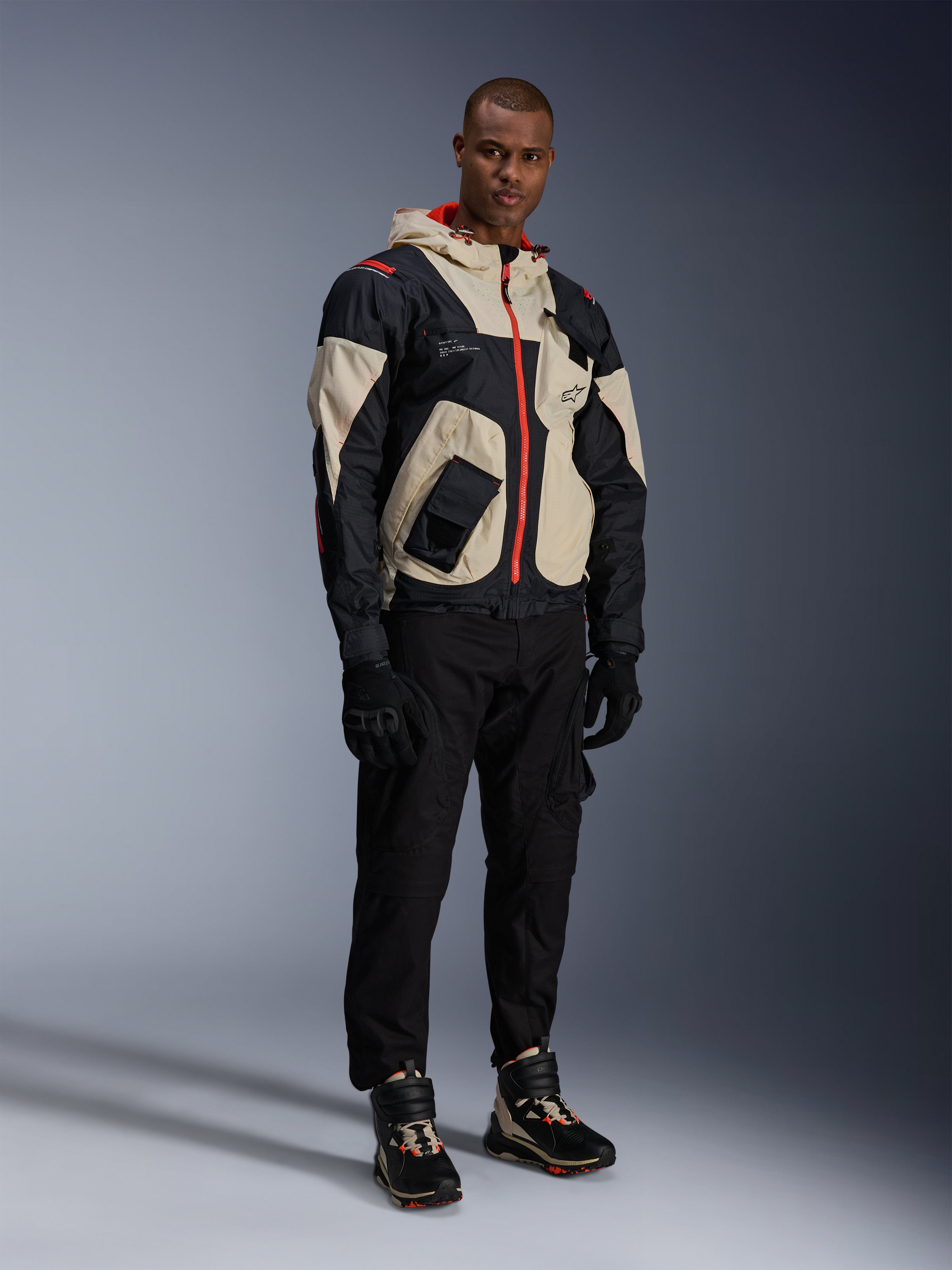 Mand i fuldt urbant motorcykeludstyr, med Alpinestars Speedstreet-sko i farven Black Almond Hot Orange og en Mogress Air-jakke i sort og creme, koordinerede sorte bukser og handsker, streetwear-inspireret beskyttende outfit til bykørsel