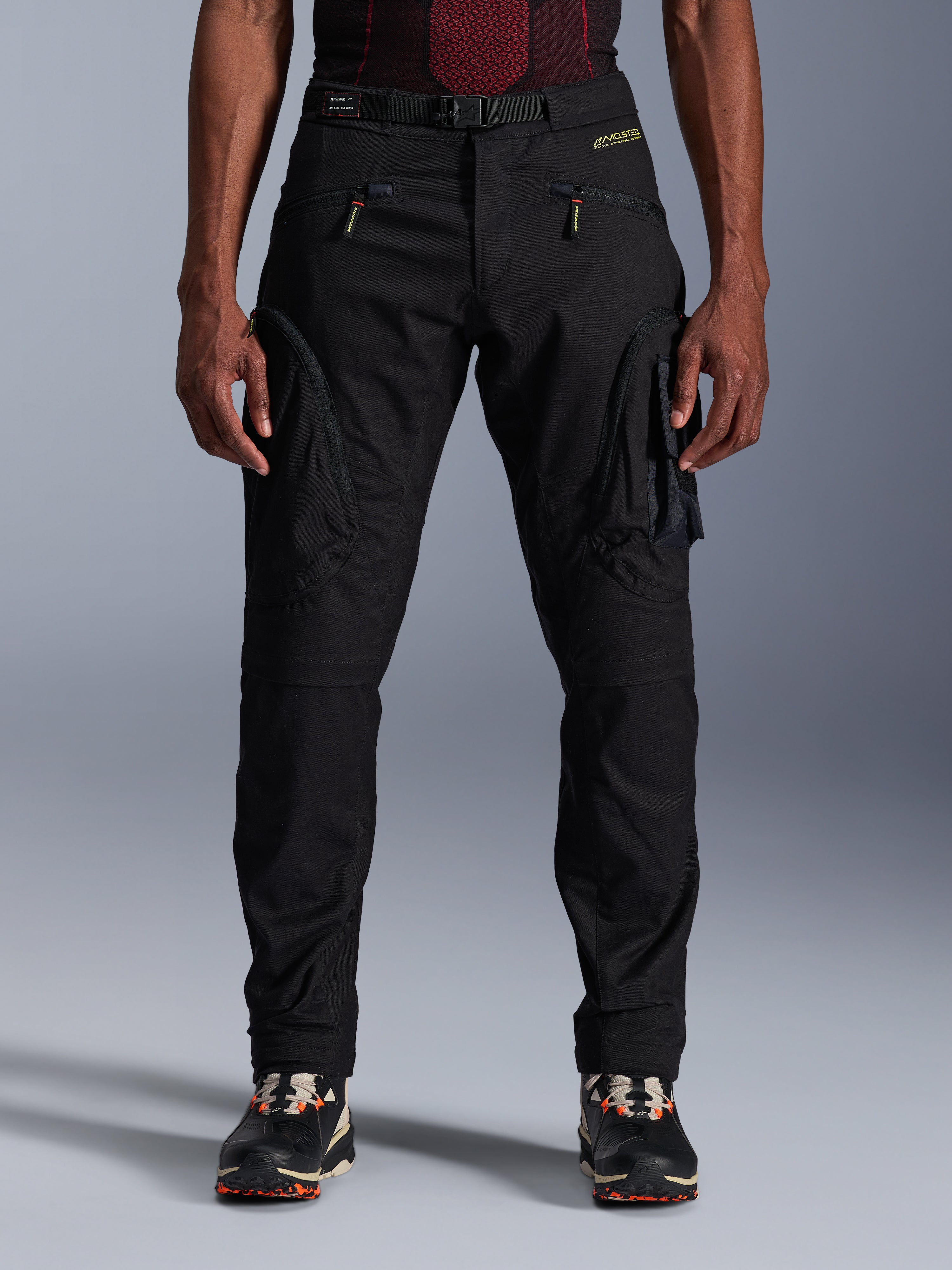 Alpinestars Acteon bukser, sorte urban motorcykelbukser, tapered regular pasform med cargolommer i siden og omvendte lynlåse, integreret bælte og gult logo, beskyttende tekstil-køreudstyr