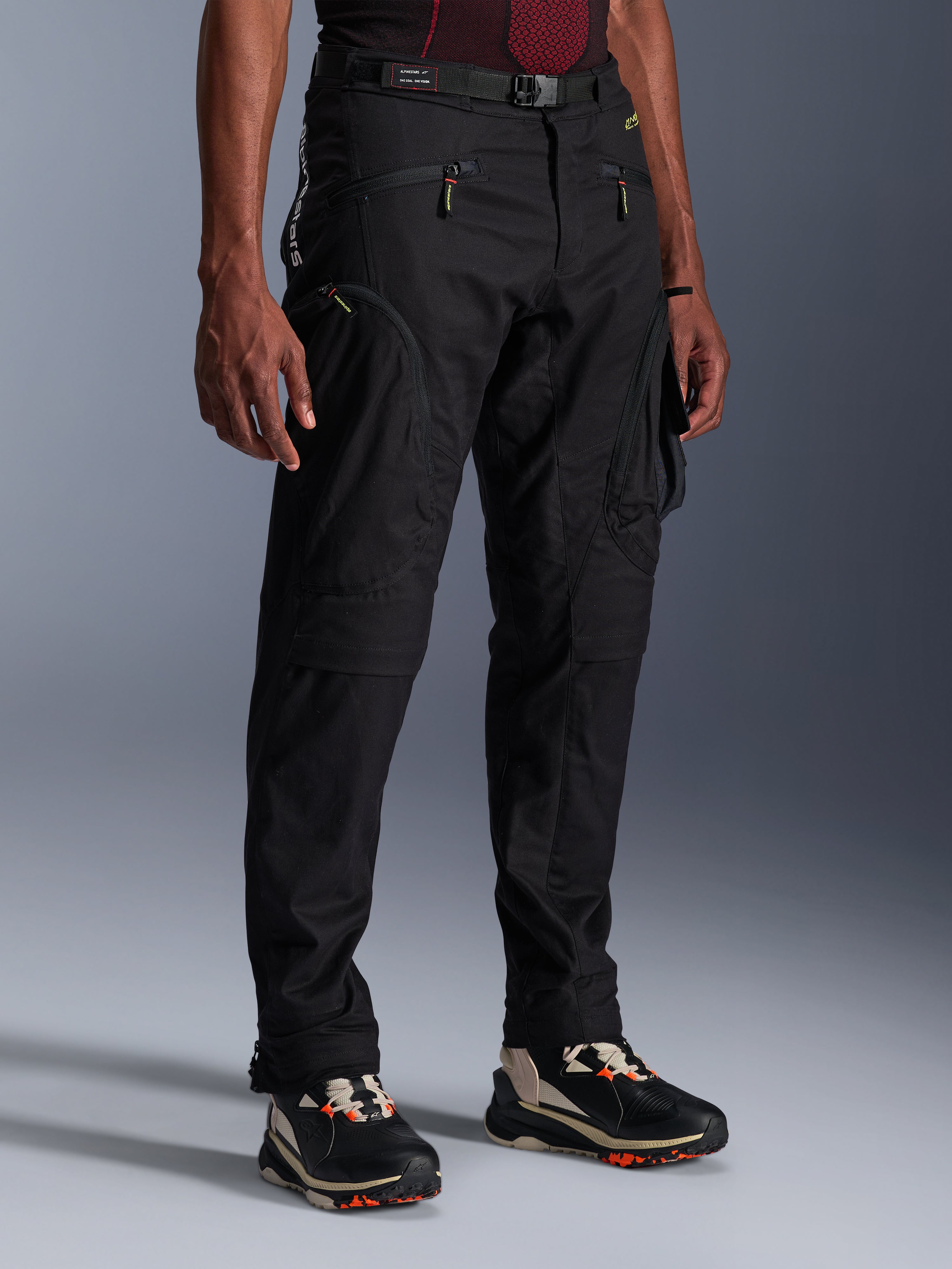 Alpinestars Acteon bukser, sorte motorcykelbukser, vist på en model, med en moderne tilspidset silhuet, cargolommer med lynlås, justerbart taljebælte og tekniske sneakers, urbant køreudstyr