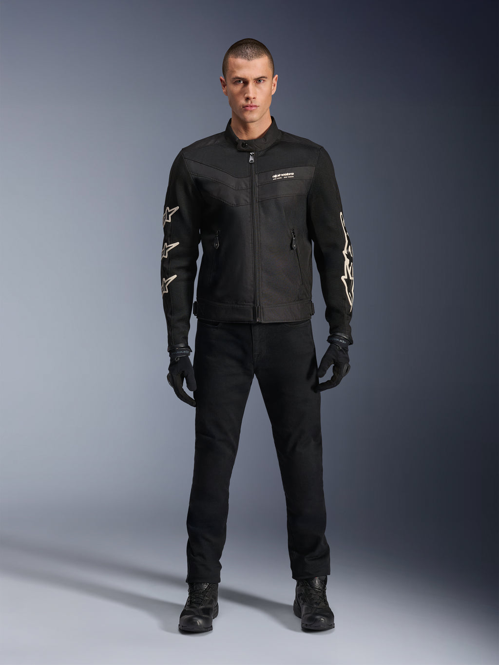 Mandlig model iført Alpinestars T-Dyno Air jakke, sort, let tekstil motorcykeljakke med åndbar 3D-mesh, hvide stjernelogoer på ærmerne, kombineret med sorte bukser, handsker og støvler, set forfra, stående