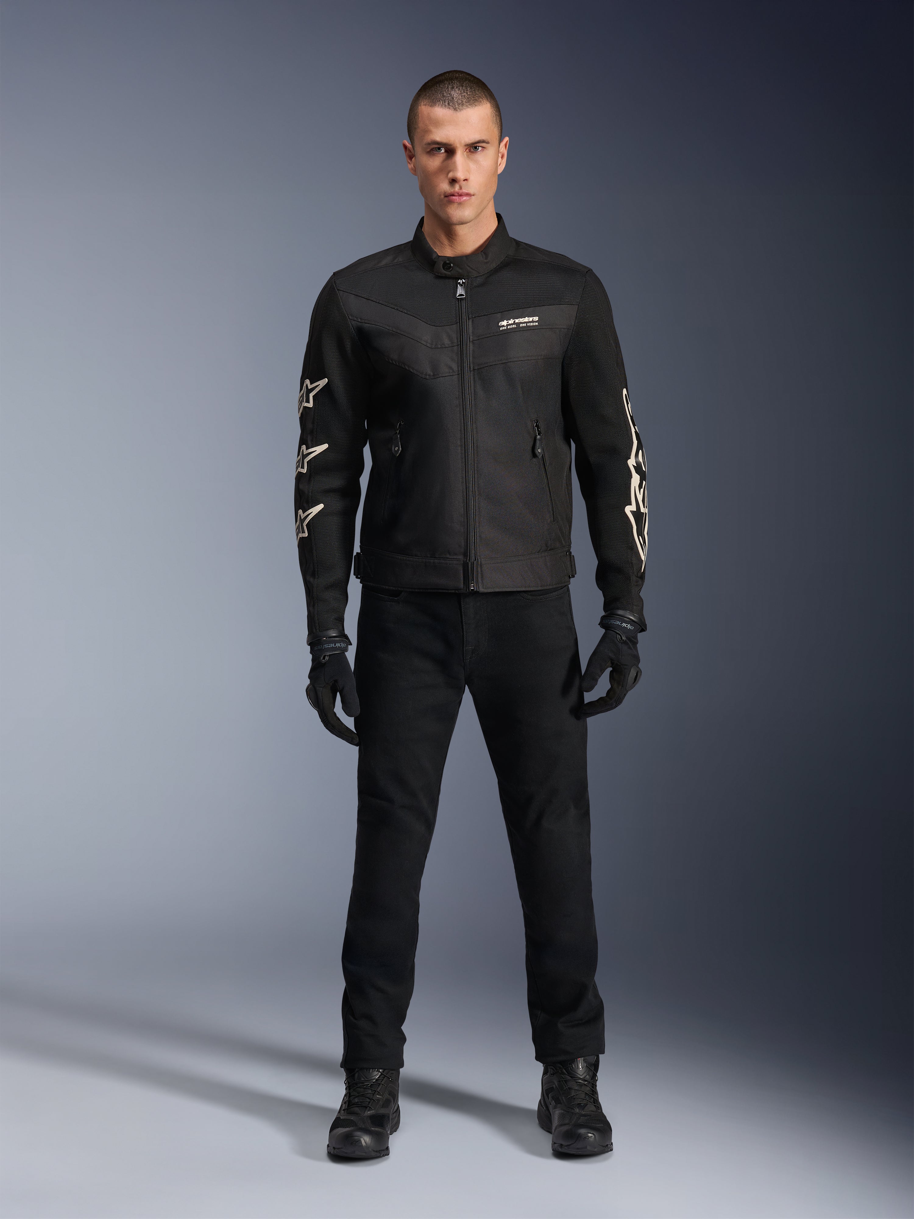 Mandlig model iført Alpinestars T-Dyno Air jakke, sort, let tekstil motorcykeljakke med åndbar 3D-mesh, hvide stjernelogoer på ærmerne, kombineret med sorte bukser, handsker og støvler, set forfra, stående