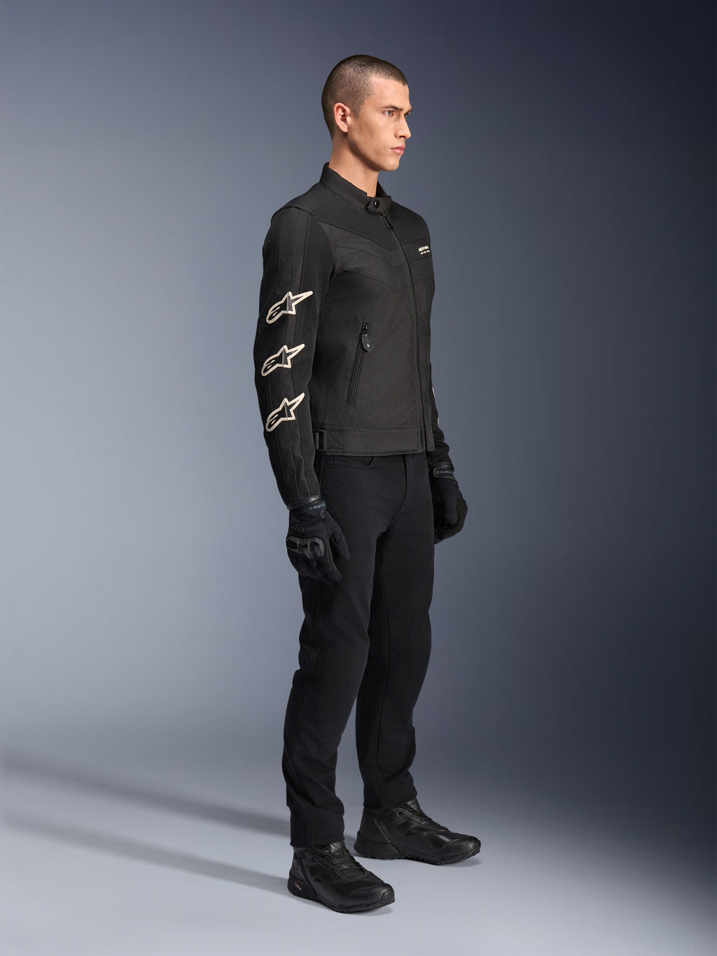 Alpinestars T-Dyno Air jakke, sort, tekstil motorcykeljakke, med tre hvide Alpinestars-logoer på ærmet, båret med matchende sorte bukser og handsker, urban køreudstyr med åndbare mesh-paneler