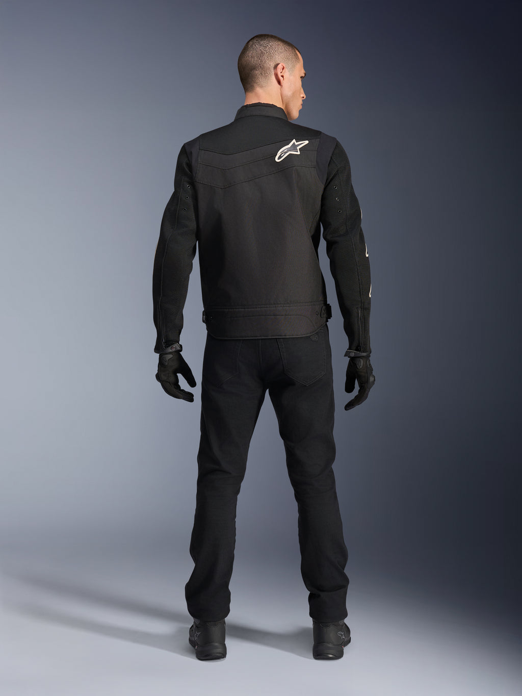Alpinestars T-Dyno Air Jakke, sort, bagfra på model, tekstil motorcykeljakke med 3D-meshpaneler og hvidt stjernelogo på skulderen, båret med sorte bukser og handsker, moderne urbant køreoutfit
