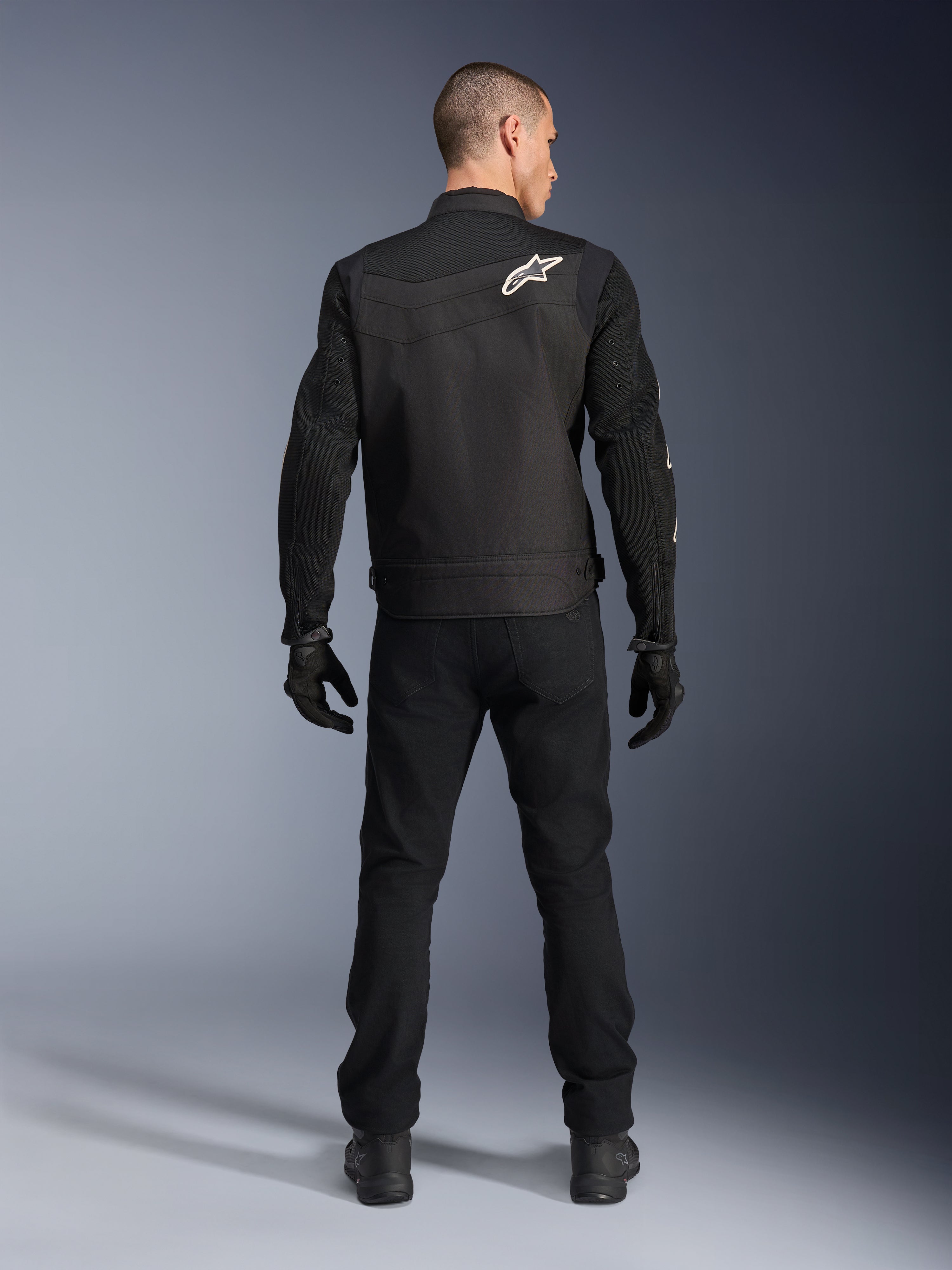 Alpinestars T-Dyno Air Jakke, sort, bagfra på model, tekstil motorcykeljakke med 3D-meshpaneler og hvidt stjernelogo på skulderen, båret med sorte bukser og handsker, moderne urbant køreoutfit