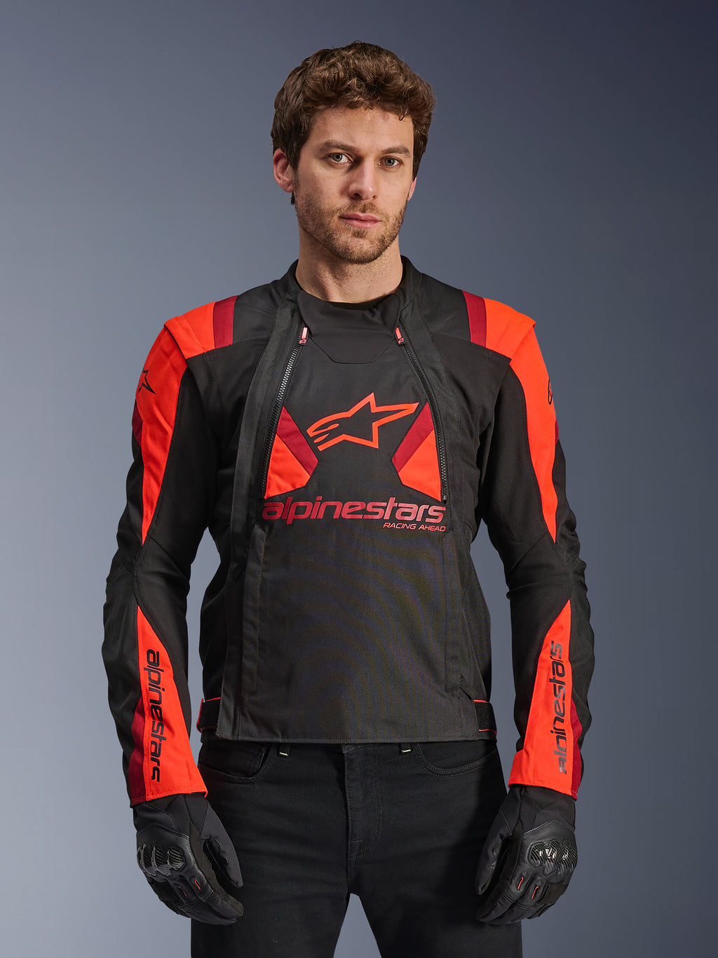Alpinestars T-Stunt Air jakke, tekstil-motorcykeljakke, sort og rød, med stort stjernelogo og mesh-paneler for luftgennemstrømning, båret af model med sorte handsker