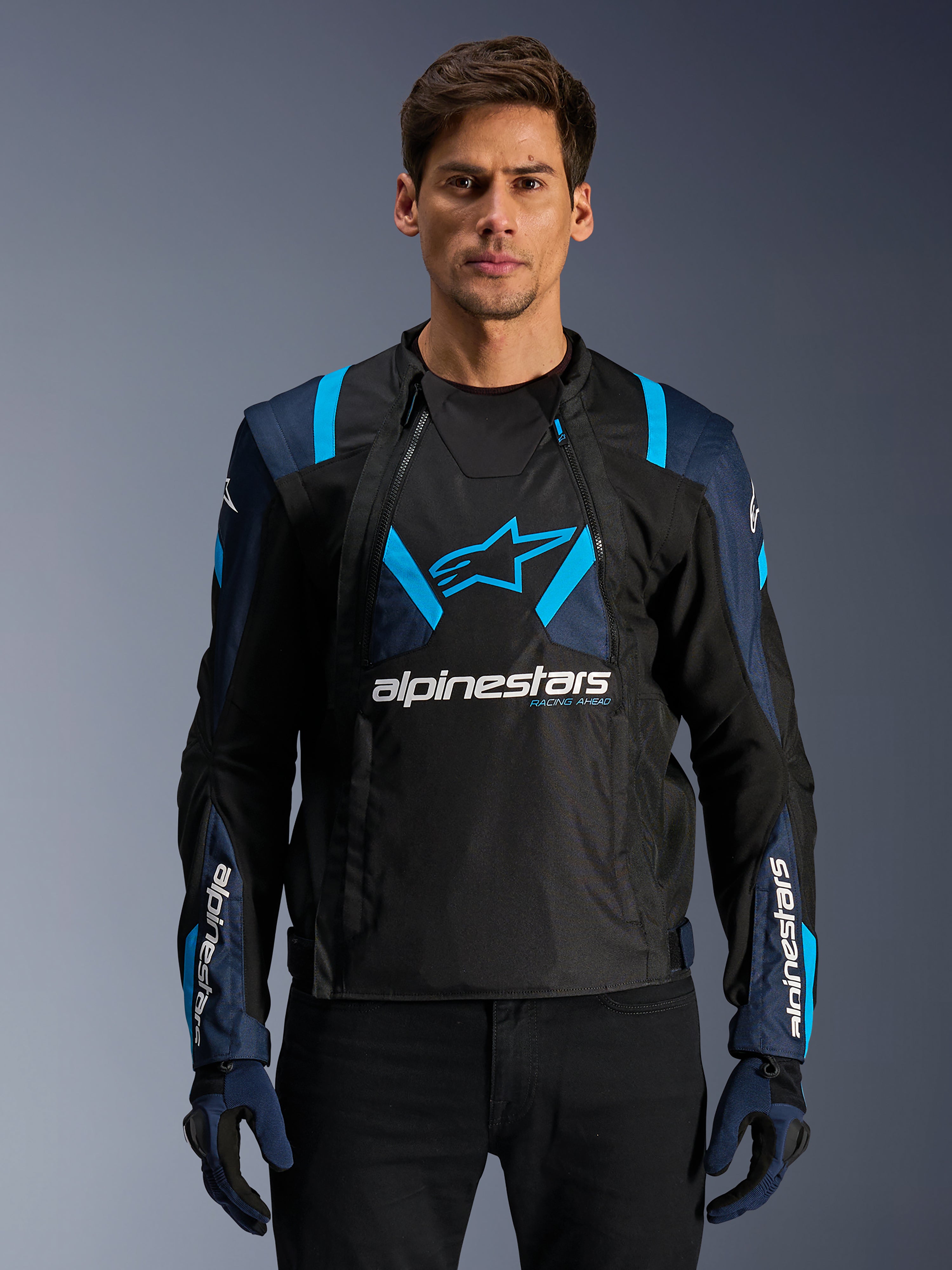 Alpinestars T-Stunt Air Jacket, motorcykel-meshjakke, sort og blå, båret af en model med sorte bukser og handsker, med et modulært 2-i-1 design med åndbare tech-meshpaneler, stjernelogo på brystet og Alpinestars-branding på ærmerne