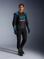 Mandlig model iført Alpinestars T-Stunt Air jakke, sort, mørkeblå og lyseblå, med fremtrædende mesh-paneler for luftgennemstrømning, kombineret med sorte bukser og kørehandsker, sportslig motorcykeljakke til sommerens landevejskørsel.