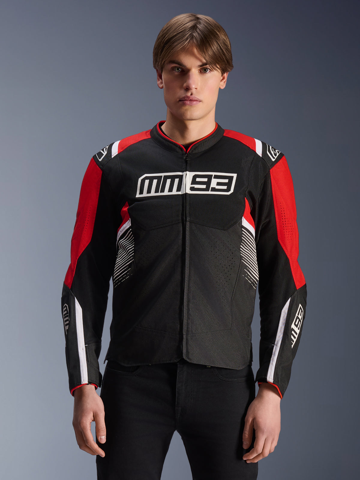 MM93 T-SPS Air V2-jakke, tekstil-motorcykeljakke i sort, klar rød og hvid, med Marc Márquez' signatur MM93-branding på bryst og ærmer, mesh-paneler til ventilation, sports-snit design, båret af model med sorte bukser