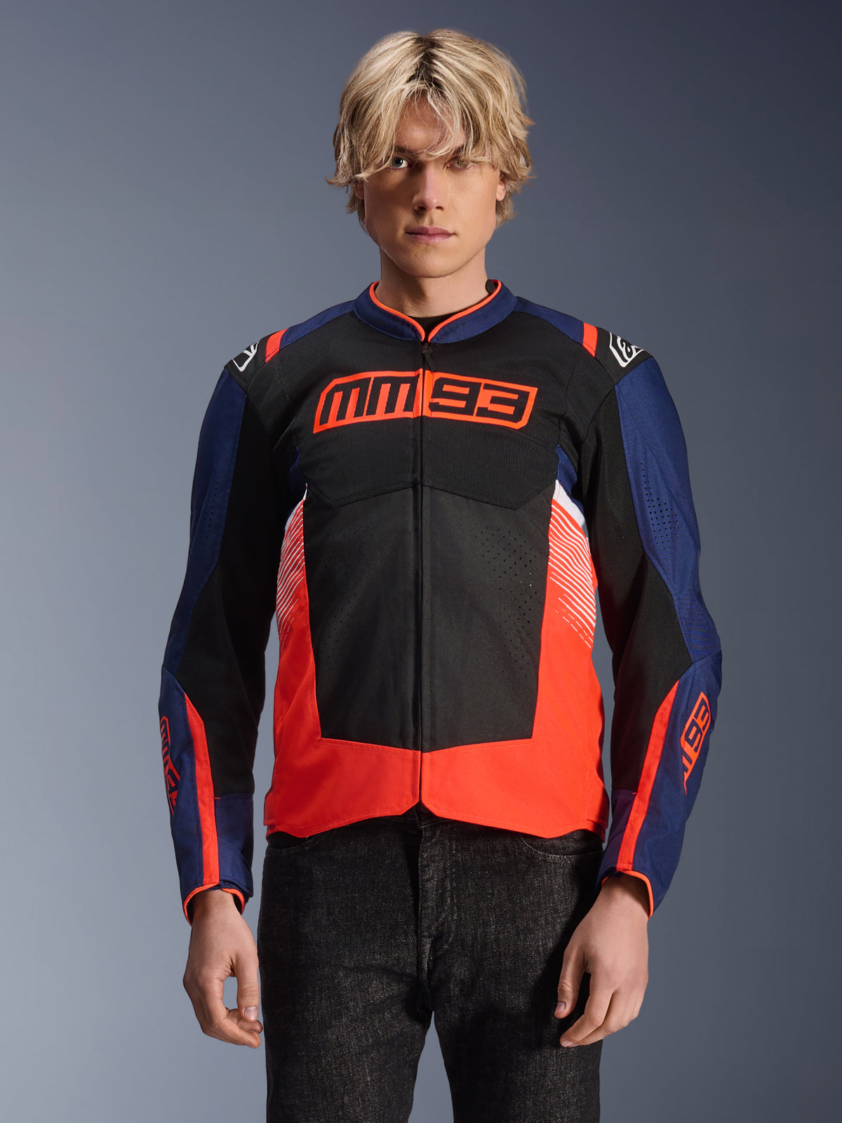 Alpinestars MM93 T-SPS Air V2-jakke, tekstil-motorcykeljakke, mørkeblå, sort og fluorescerende rød, båret af en person, med markant MM93-branding på brystet, mesh-paneler til ventilation og moderne farveopdelt design