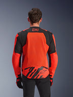 Alpinestars MM93 T-SPS Air V2 jakke, set bagfra, rød fluo og sort, med 93-racinglogo i nakken, stort mesh-panel på ryggen for luftgennemstrømning, flap nederst på ryggen med Alpinestars-stjernelogo og geometriske striber, vist med sorte bukser og kørehandsker.
