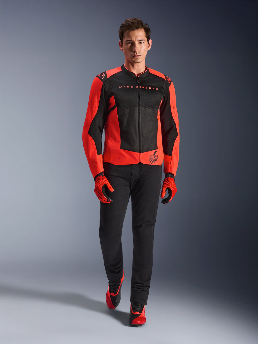 Alpinestars MM93 T-SPS Air V2 jakke, rød fluo og sort, båret af en model med matchende røde handsker og sorte bukser, med Marc Marquez-branding og 93-logo, ventileret sportsmotorcykeljakke til bykørsel