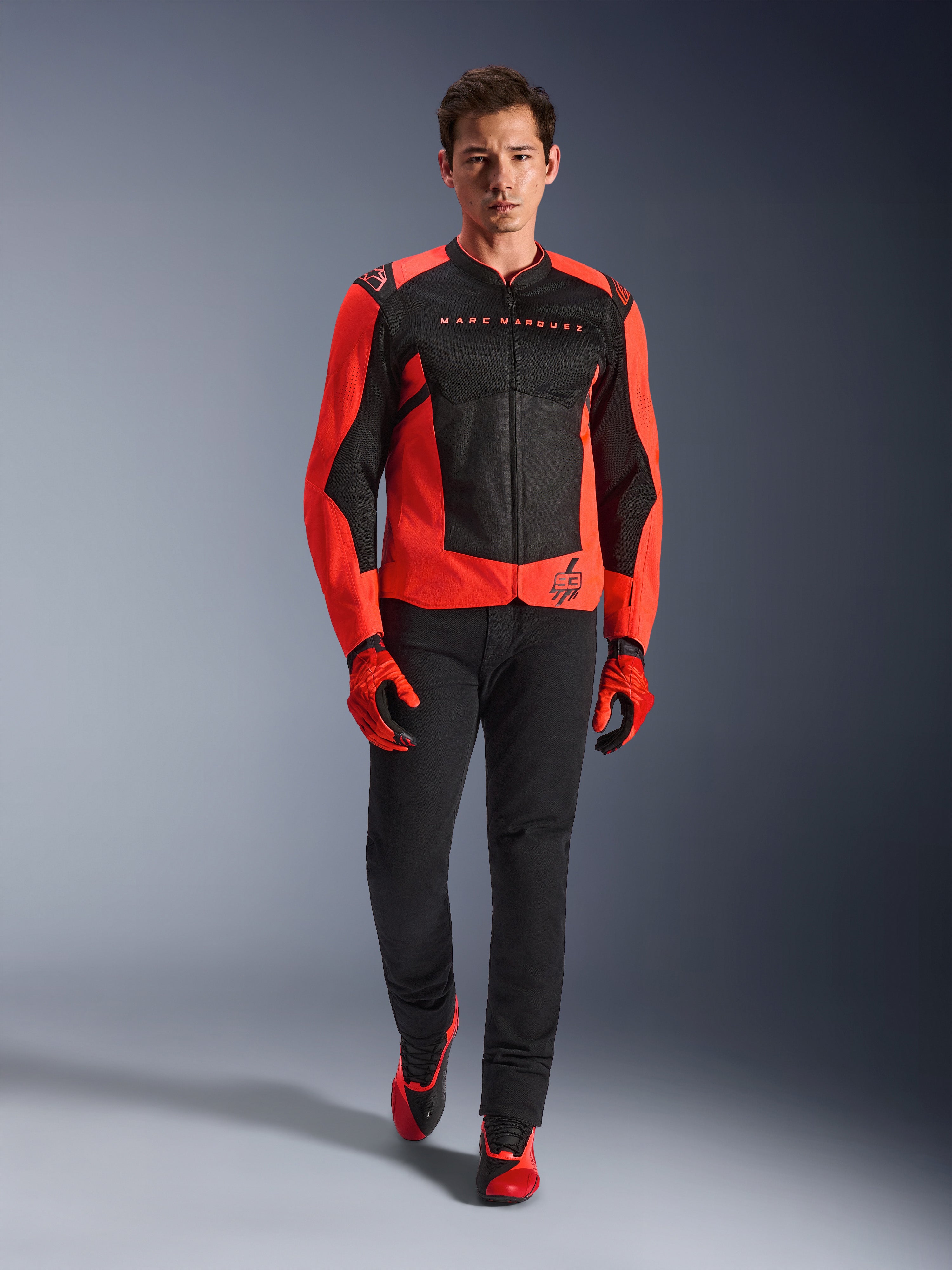 Alpinestars MM93 T-SPS Air V2 jakke, rød fluo og sort, båret af en model med matchende røde handsker og sorte bukser, med Marc Marquez-branding og 93-logo, ventileret sportsmotorcykeljakke til bykørsel