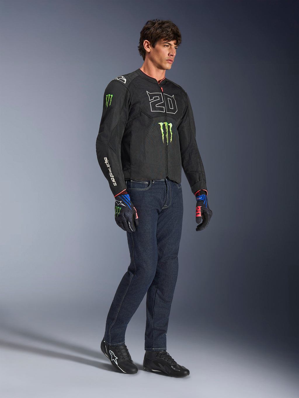 Mandlig motorcyklist iført Alpinestars FQ20 T-SPS Air V2 Monster-jakke i sort, med '20'-logo og Monster Energy-klo på brystet, kombineret med mørke motorcykeljeans, sorte motorcykelsko og matchende FQ20-handsker, studieoptagelse i fuld figur