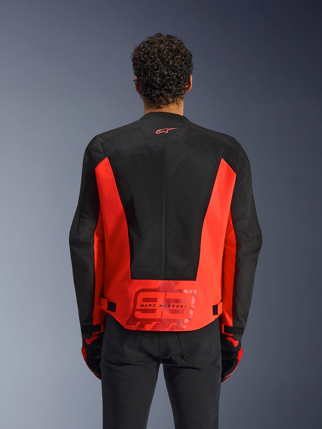Alpinestars MM93 C-1 Air-jakke set bagfra, Red Fluo og sort, mand iført jakke med et stort '93' Marc Marquez-logo på lænden, letvægts mesh-paneler til ventilation, kombineret med sorte bukser og handsker.