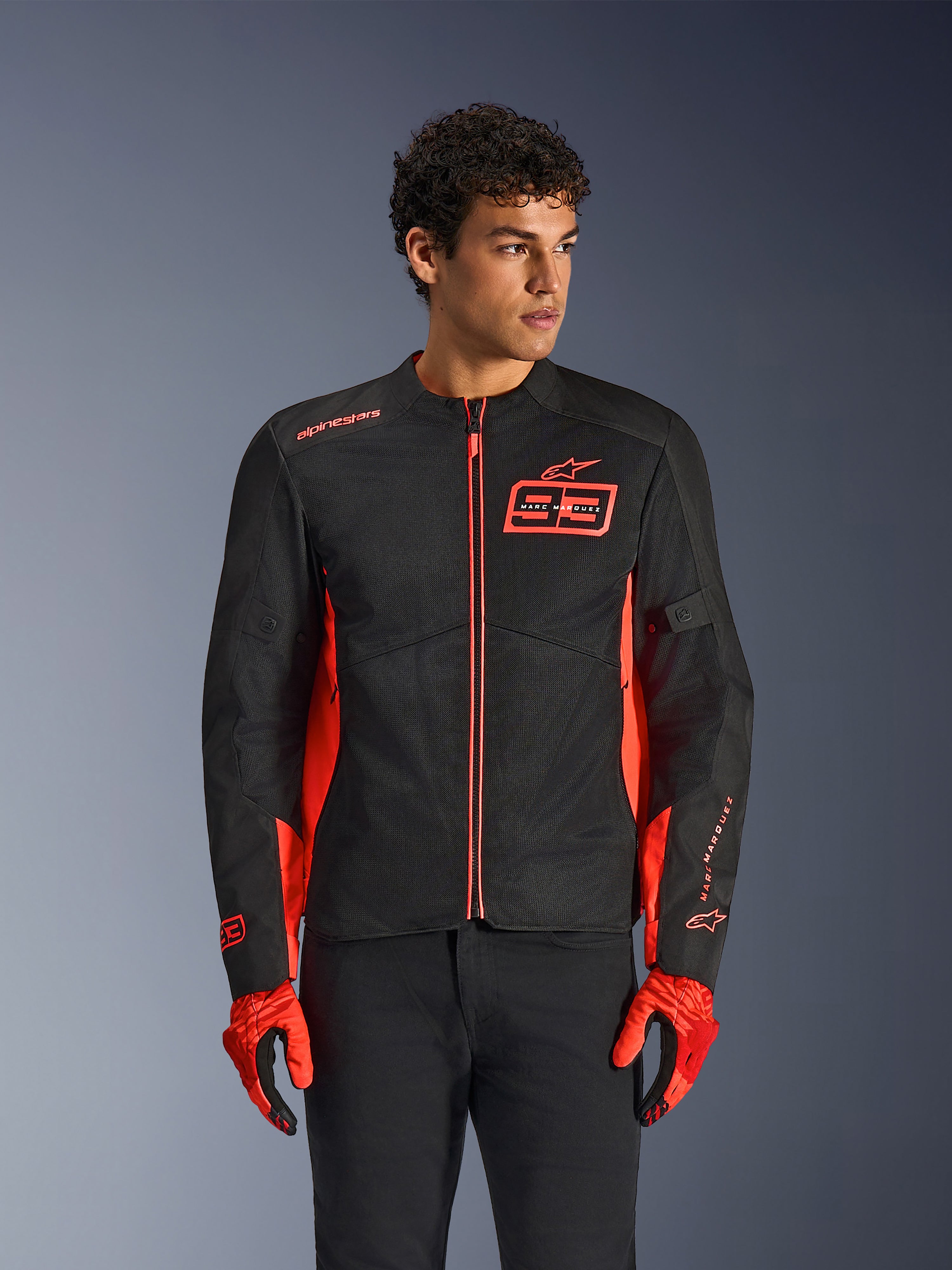 Alpinestars MM93 C-1 Air jakke, urban motorcykeljakke, Red Fluo og sort, båret af en model med matchende røde handsker og sorte bukser, med et markant 93 Marc Marquez-logo på brystet og mesh-paneler til luftgennemstrømning