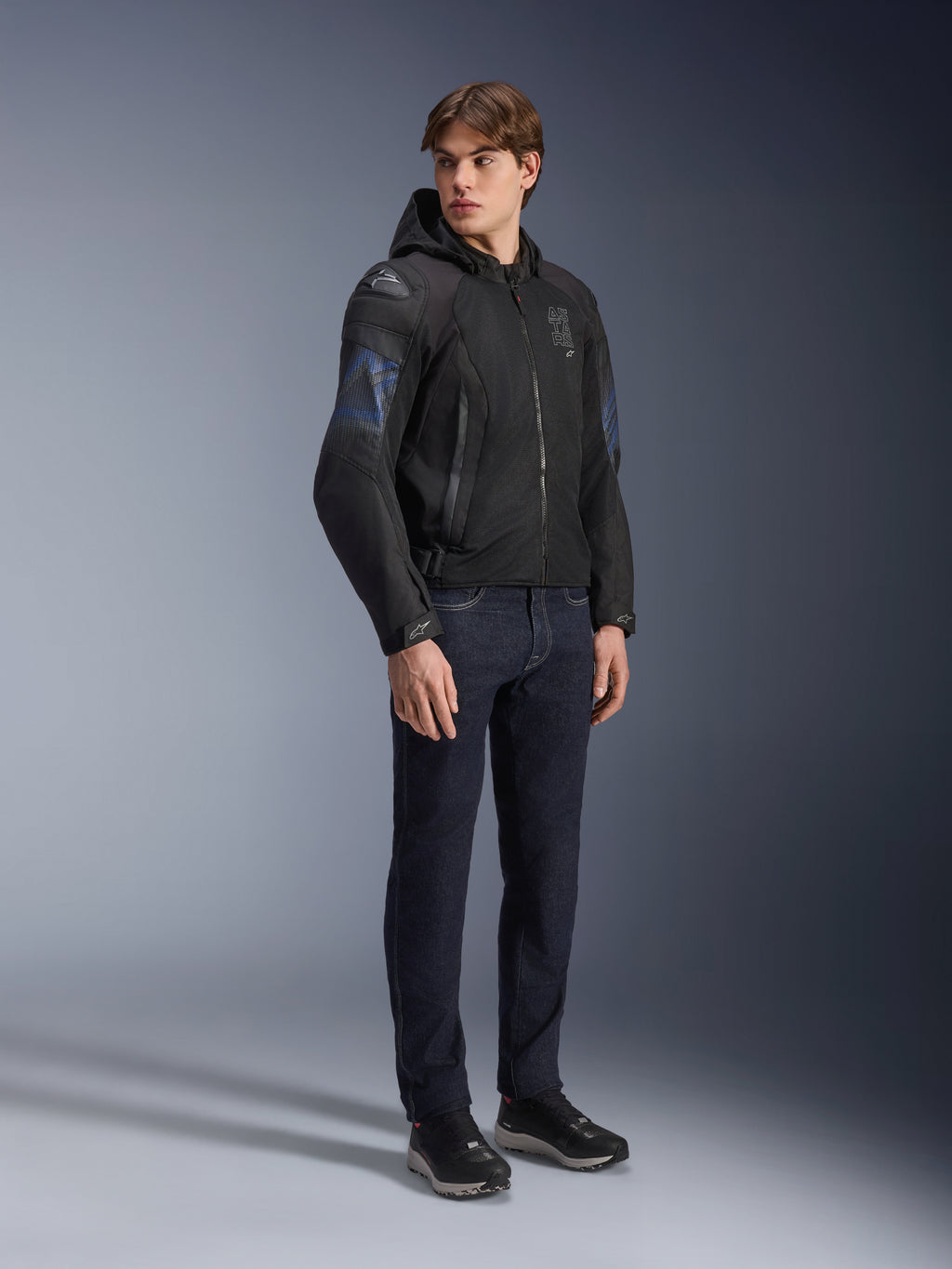 Alpinestars Zaca Air Venom WP Jacket, Black and Electric Blue textile motorcycle jacket, worn by model with dark jeans and black sneakers, featuring a detachable hood, mesh ventilation panels, and DFS Lite shoulder sliders, sporty all-weather riding gear.