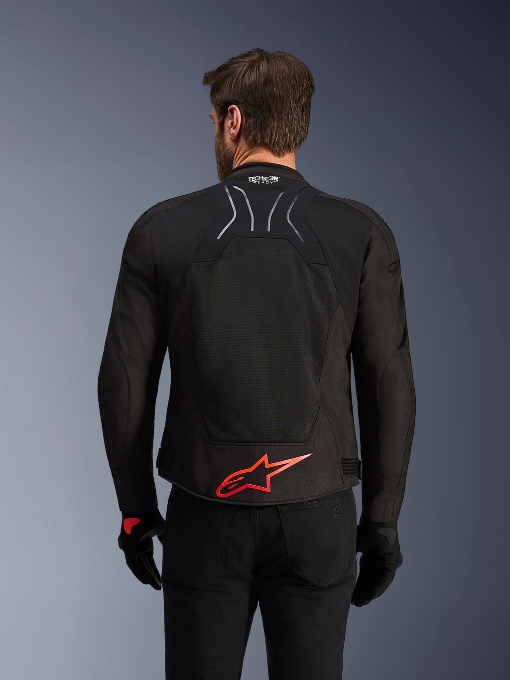 Alpinestars SMX Air-jakke, set bagfra, sort med lysende rødt Alpinestars-logo på lænden, tech-mesh-panel med høj luftgennemstrømning, Tech-Air Ready-branding, båret af en mandlig kører med sorte bukser og handsker