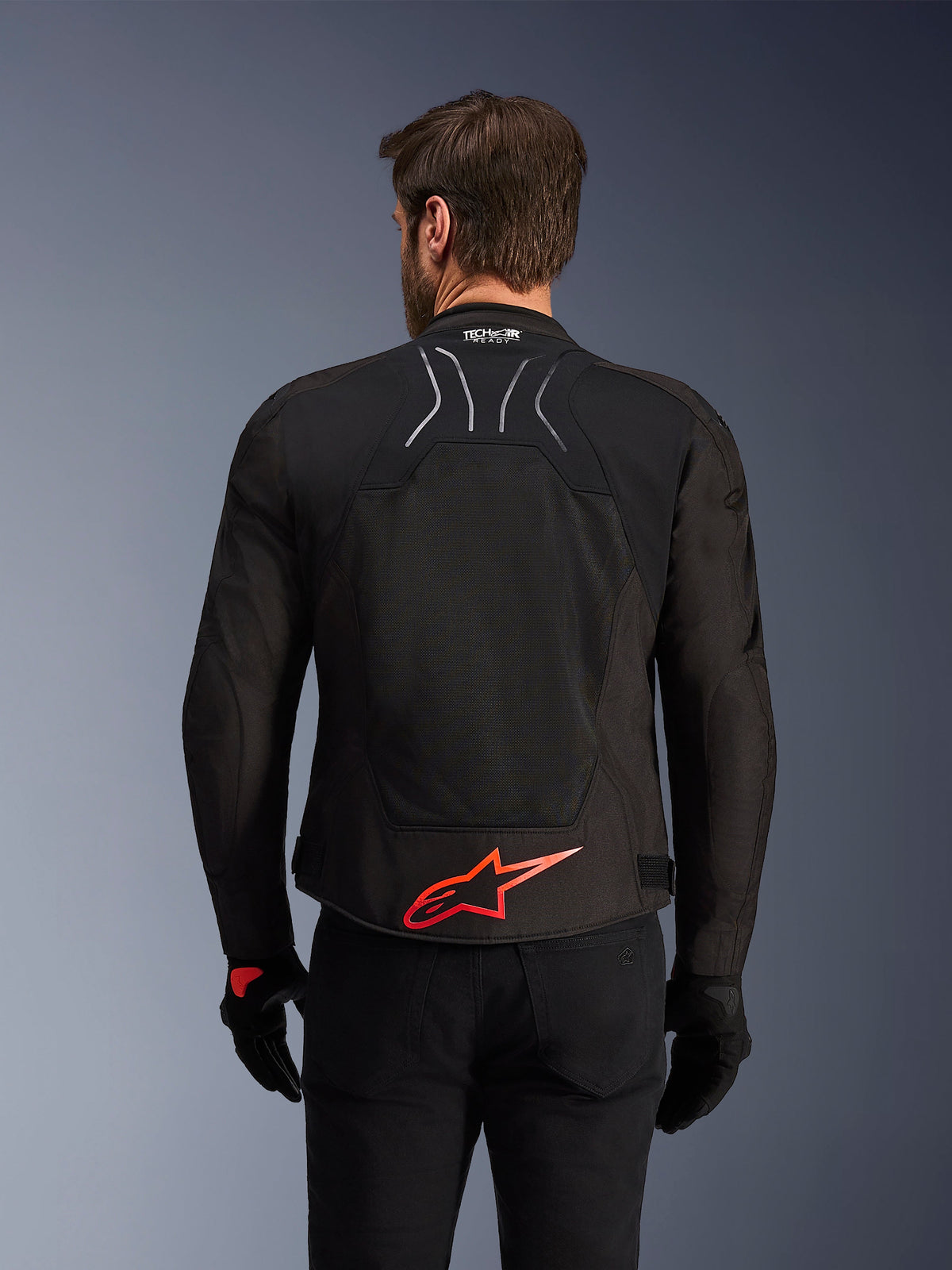 Alpinestars SMX Air-jakke, set bagfra, sort med lysende rødt Alpinestars-logo på lænden, tech-mesh-panel med høj luftgennemstrømning, Tech-Air Ready-branding, båret af en mandlig kører med sorte bukser og handsker