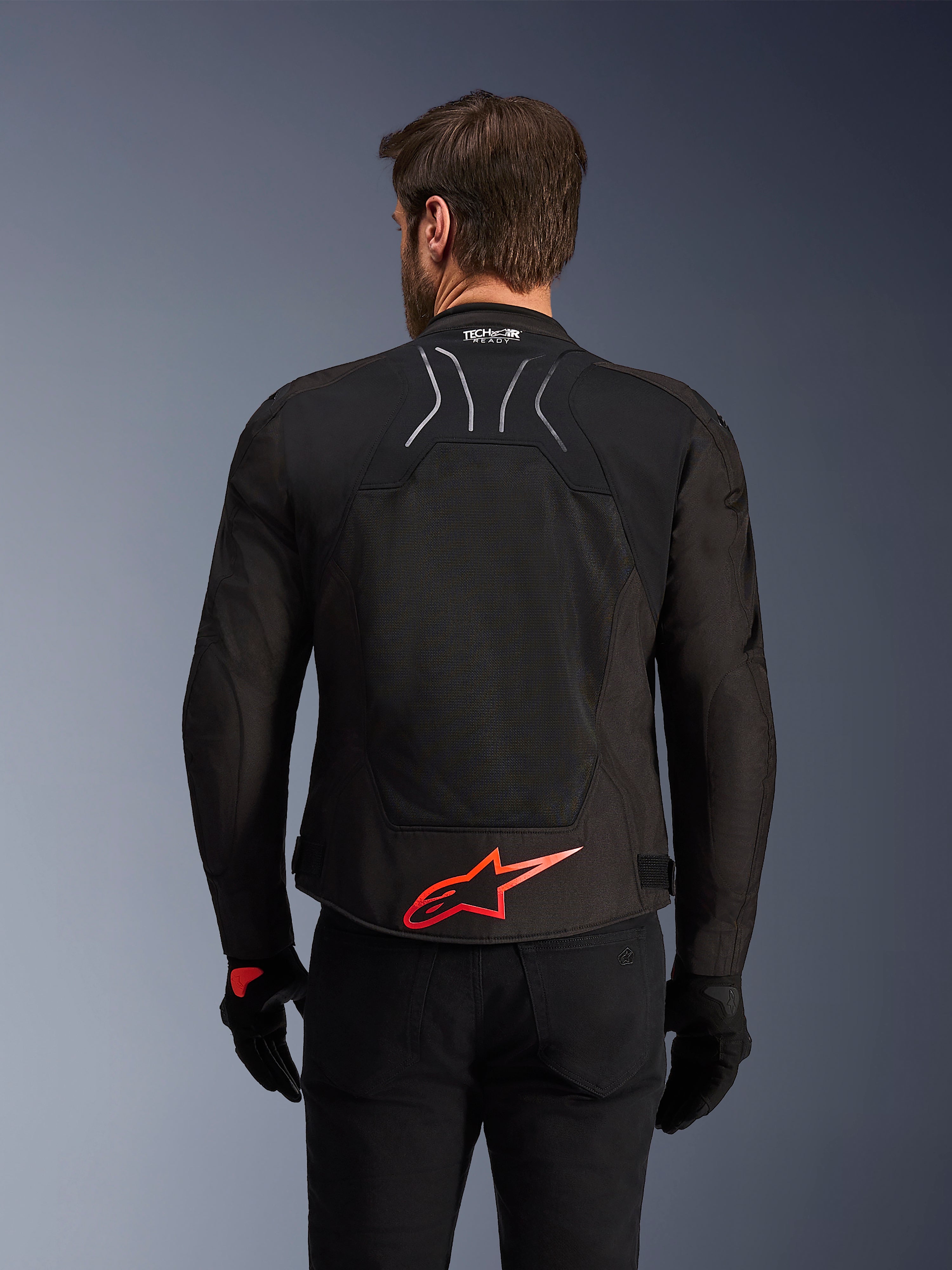 Alpinestars SMX Air-jakke, set bagfra, sort med lysende rødt Alpinestars-logo på lænden, tech-mesh-panel med høj luftgennemstrømning, Tech-Air Ready-branding, båret af en mandlig kører med sorte bukser og handsker