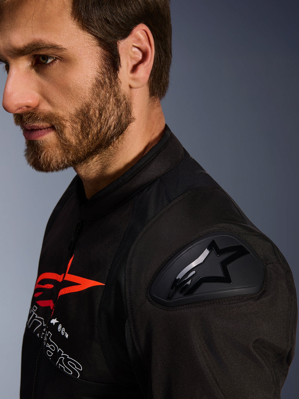 Alpinestars SMX Air jakke, sort og rød, nærbillede af DFS Lite skulderbeskytter med stjernelogo, båret af en mand med skæg, tekstil racing- og sportsmotorcykeljakke