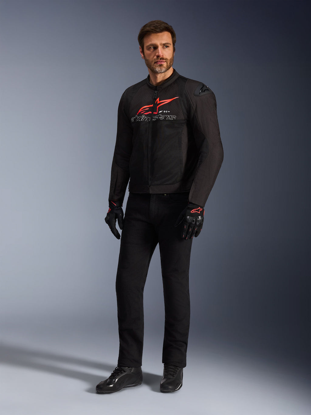 Mandlig model iført Alpinestars SMX Air-jakke i Black Bright Red White, kombineret med sorte tekniske bukser, sort-røde handsker og sorte køresko, med et markant rødt brystlogo og hvid branding, helkropsstudiebillede af sportsmotorcykeludstyr
